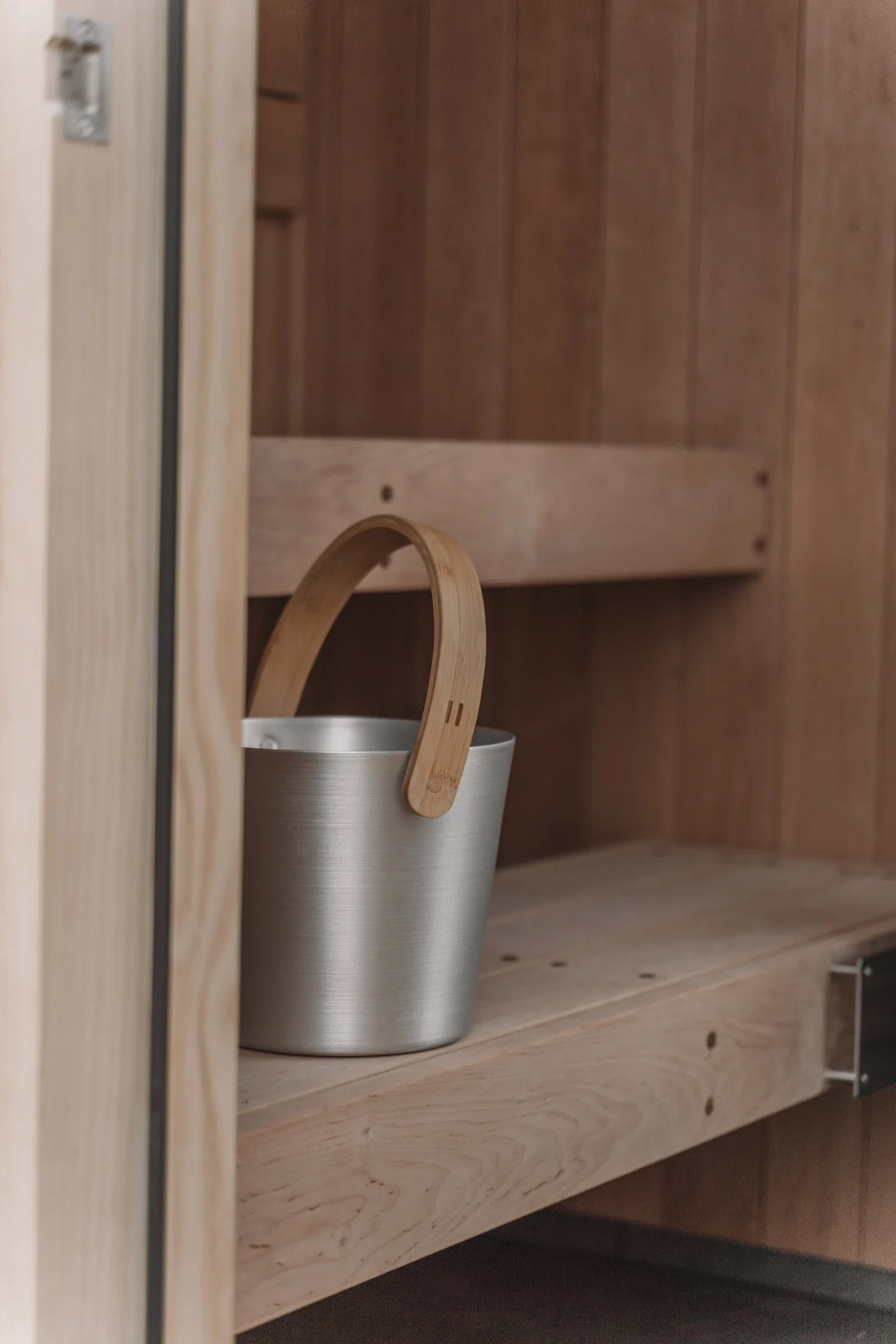 A metal bucket with a wooden handle inside a wooden cupboard.