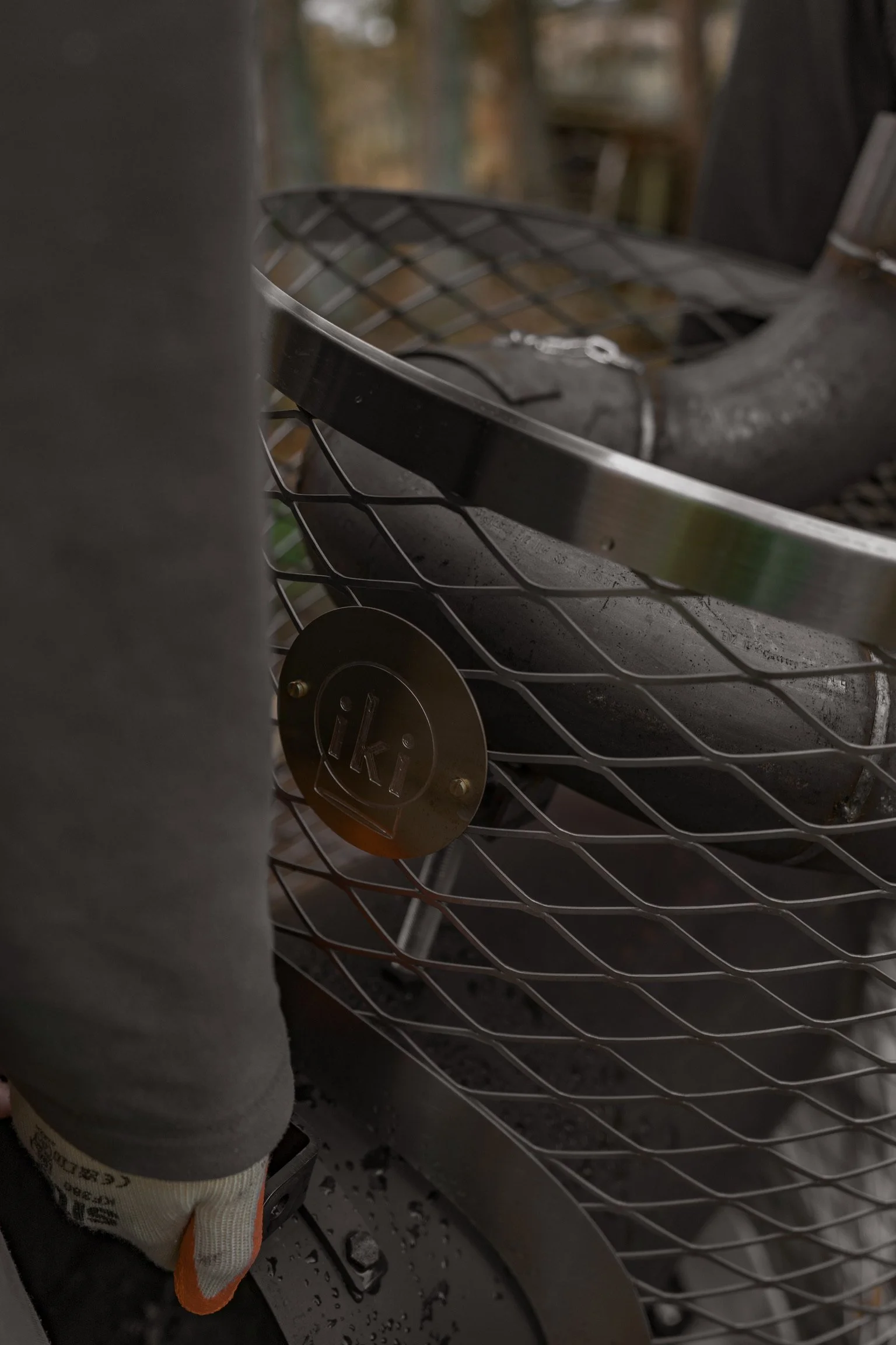Close-up of a black grill with the brand logo 'iKI' on a metal plate, showing the grate and some ashes inside.
