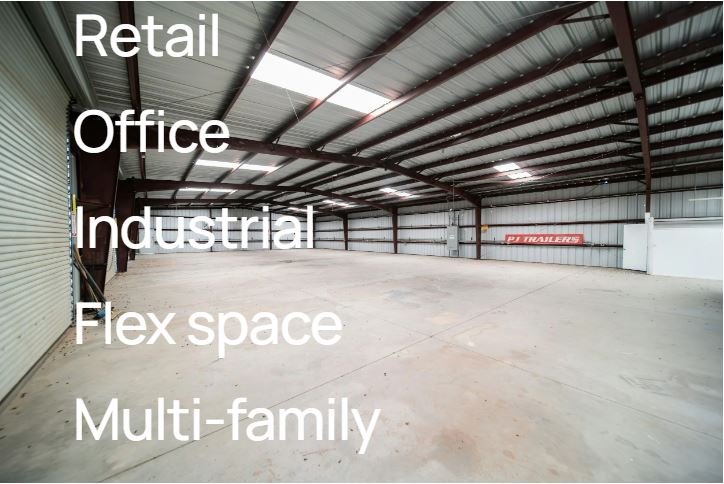 Empty large warehouse with metal ceiling supports and concrete floor, signage for various commercial uses such as retail, office, industrial, flex space, and multi-family.