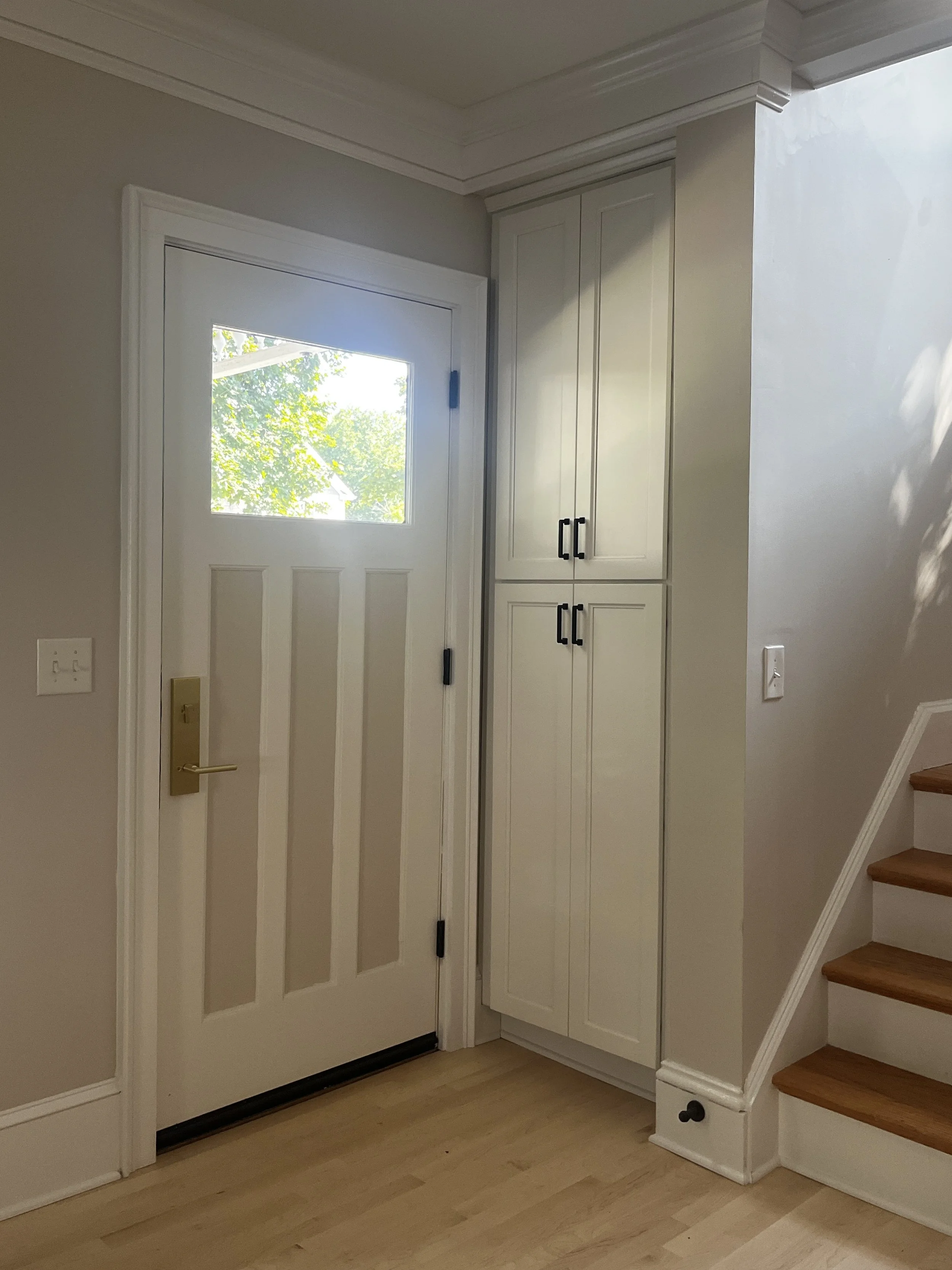 custom entryway door with two tone paint applied to it featuring a window, alongside white built-in cabinets 