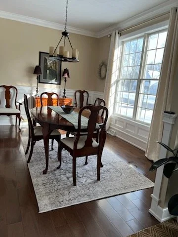 White wainscoting on a wall with a framed artwork above, and a wooden floor with a decorative vent cover on the floor.