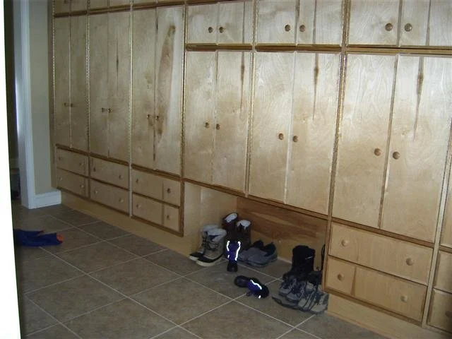 Mudroom birch plywood faced and structured built-in cabinets and drawers with shoes on the tiled floor underneath.