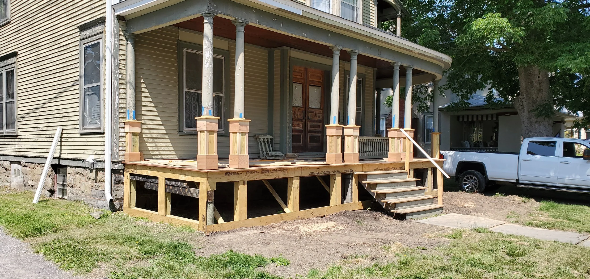 Front porch of a house under construction with wooden posts and stairs, reconstructed columns for design and support.