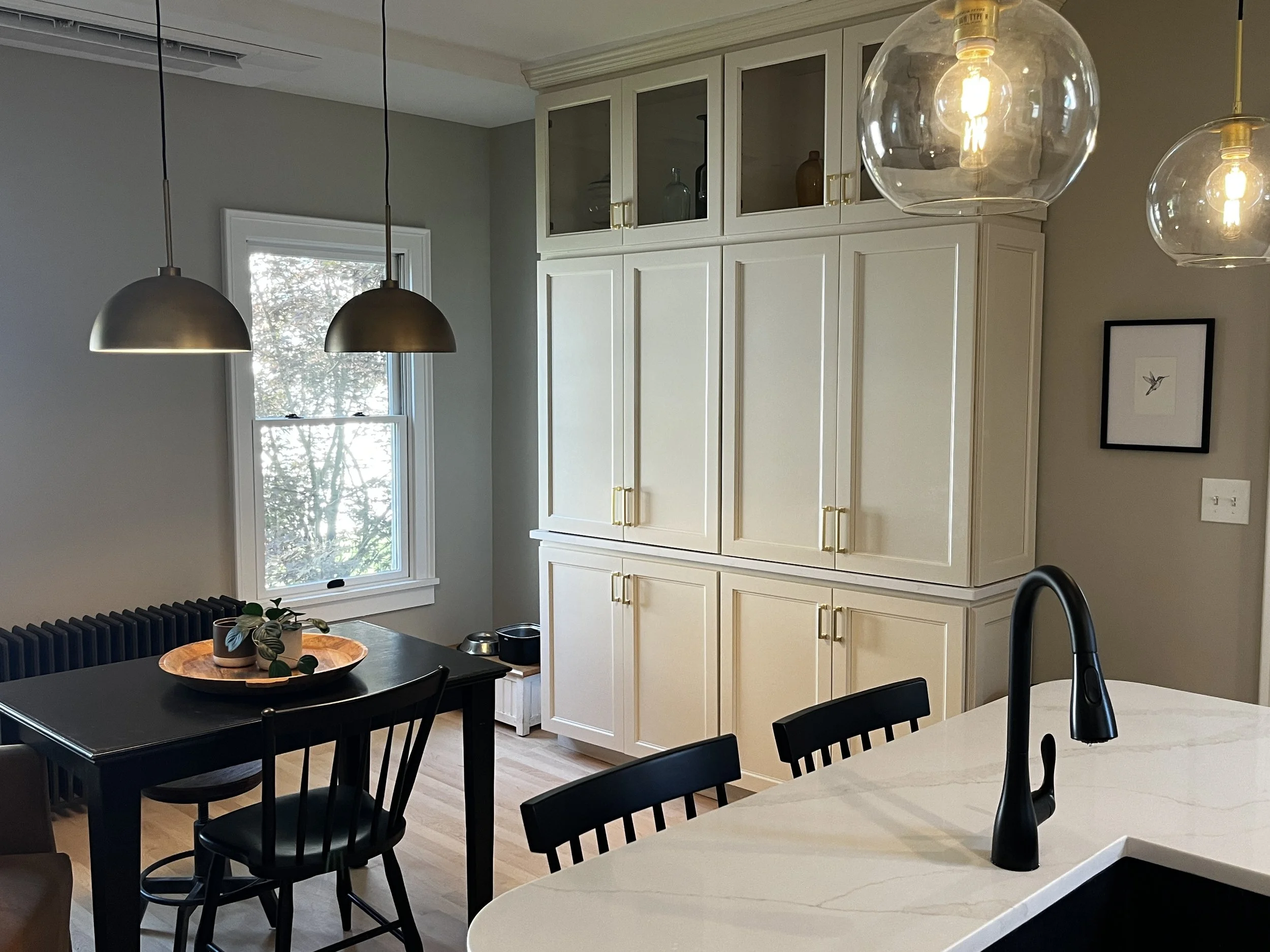 Modern kitchen with white cabinetry, black dining table with chairs, pendant lights, and a marble countertop with a black faucet.