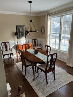 Dining room with wooden table, six chairs, chandelier, large window, and wall art.