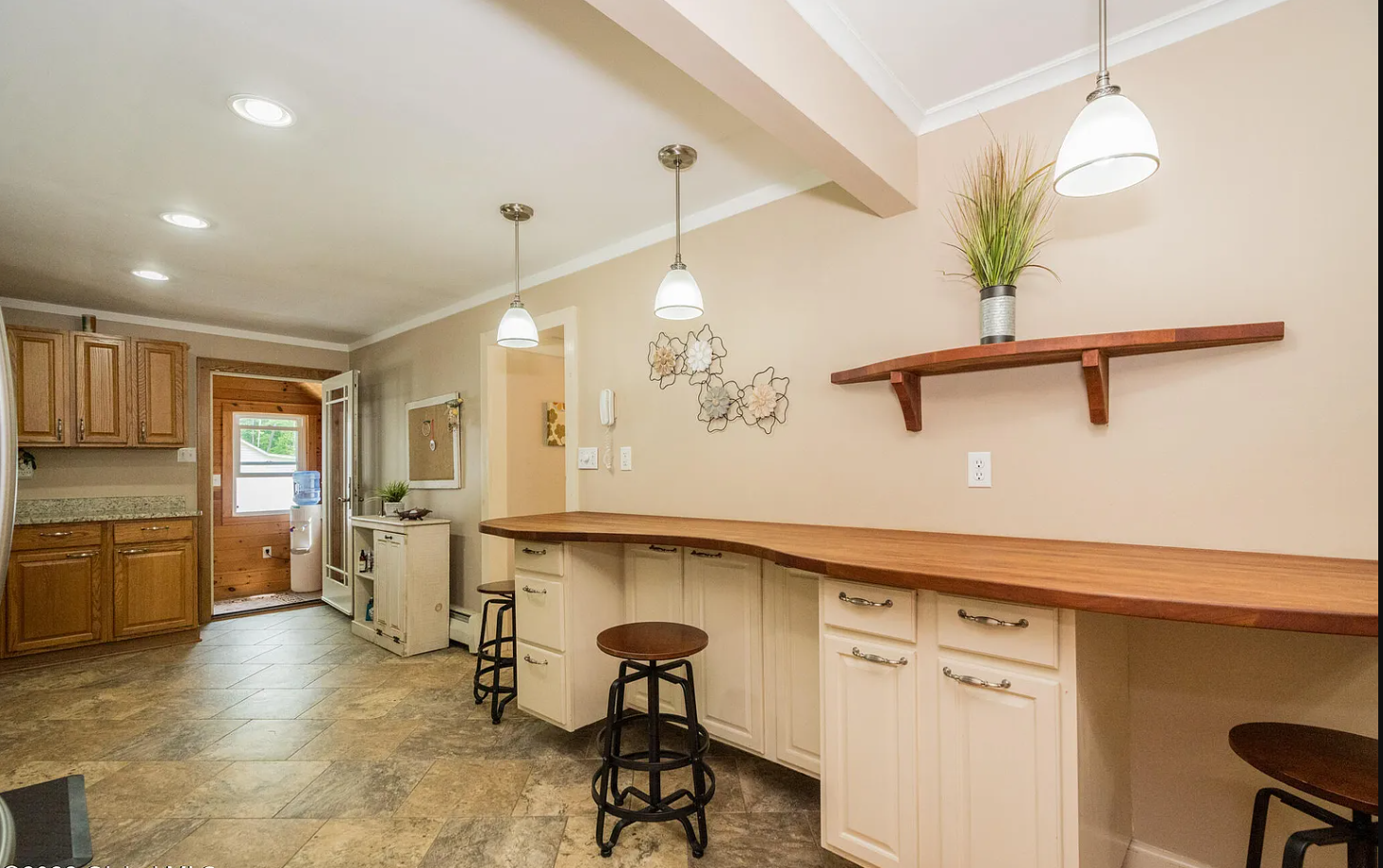 Kitchen with wood and cream cabinets, wooden countertops, tile floor, pendant and recessed lighting, wall decoration, and a small breakfast bar with stools.