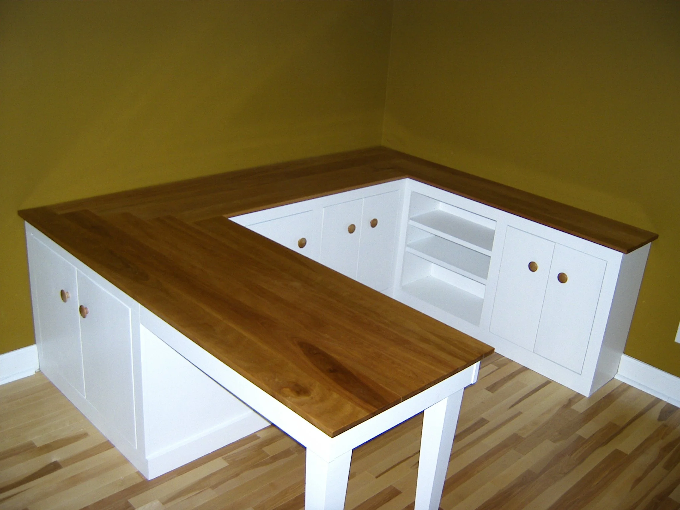 Kitchen countertop with white cabinets and open shelves, corner layout, on wooden flooring, with mustard yellow wall.