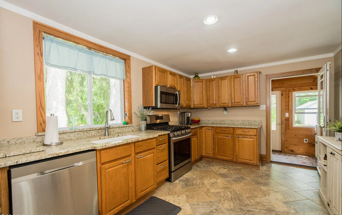 Kitchen with wooden cabinets, granite countertops, stainless steel appliances, a window above the sink, and a door leading outside.