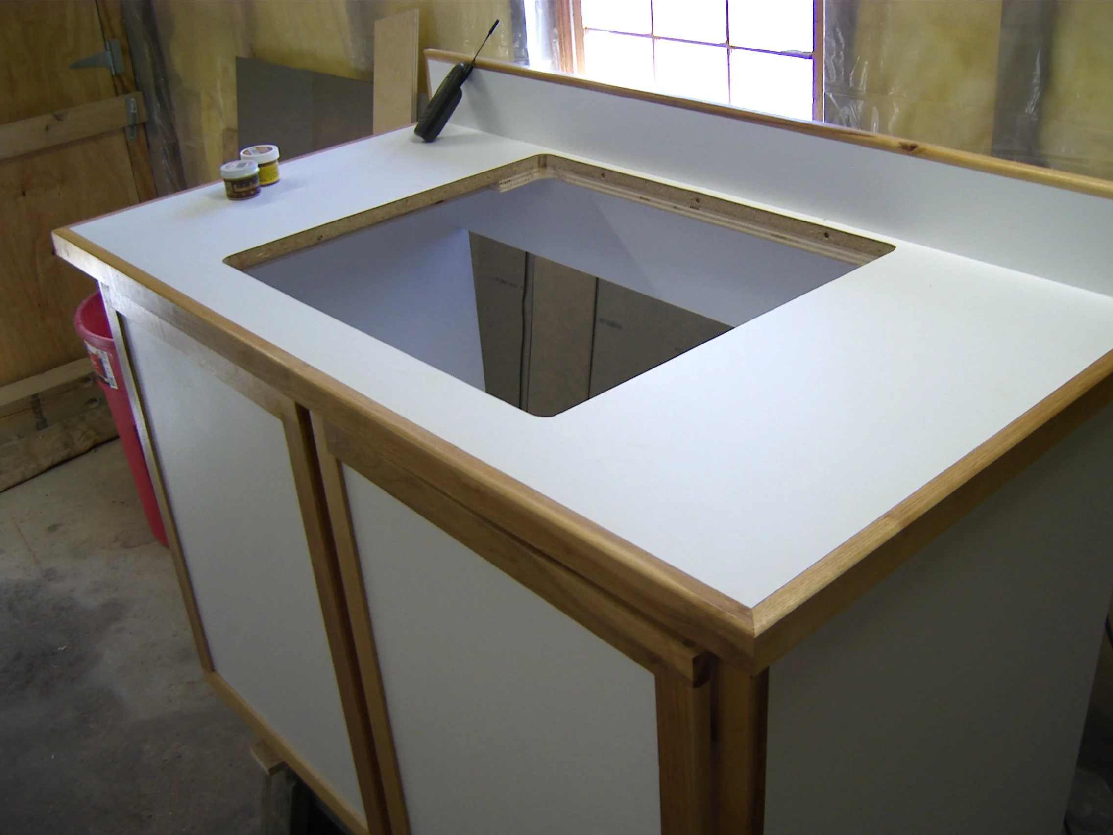 Kitchen countertop with a hole for a sink, two jars of materials, and a putty knife, indoors with a window.