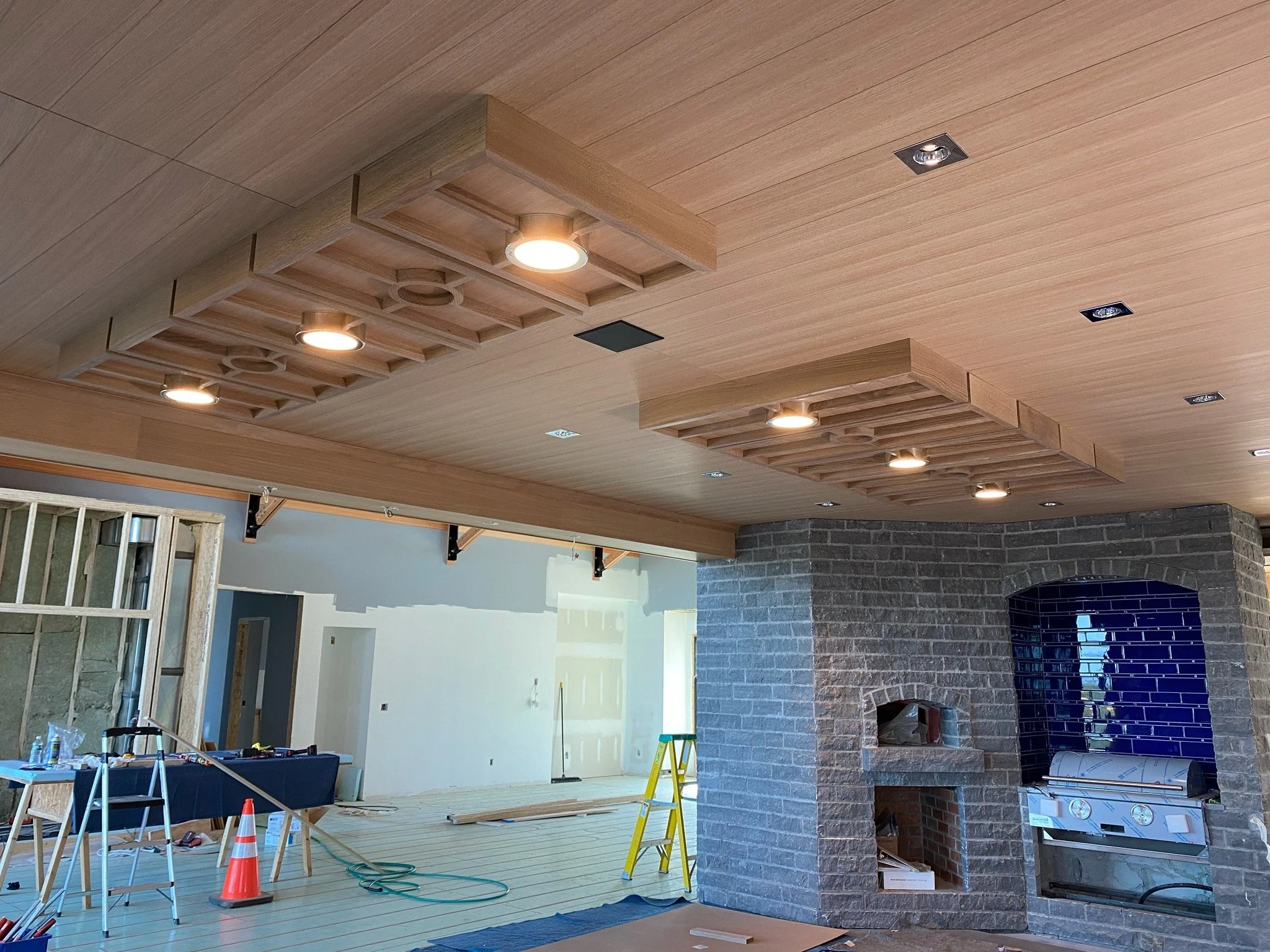 Interior of a room under construction featuring a wooden ceiling with built-in lights, a brick fireplace, and construction tools and materials