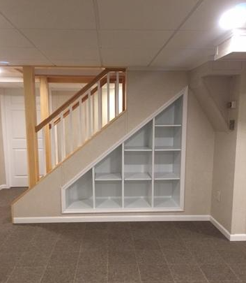 Built-in triangular bookshelf under a staircase with wooden handrails.base trimmed with regular casing