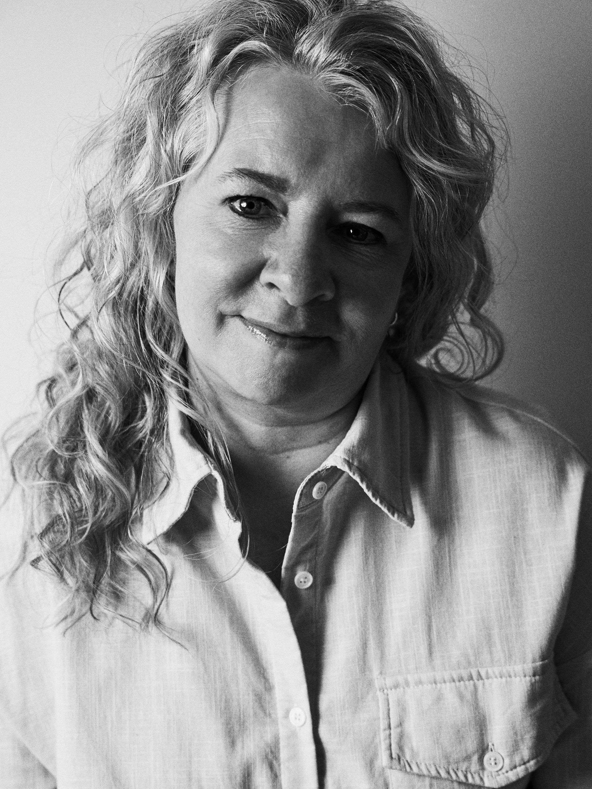 Black and white close-up portrait of a woman with curly hair wearing a button-up shirt.