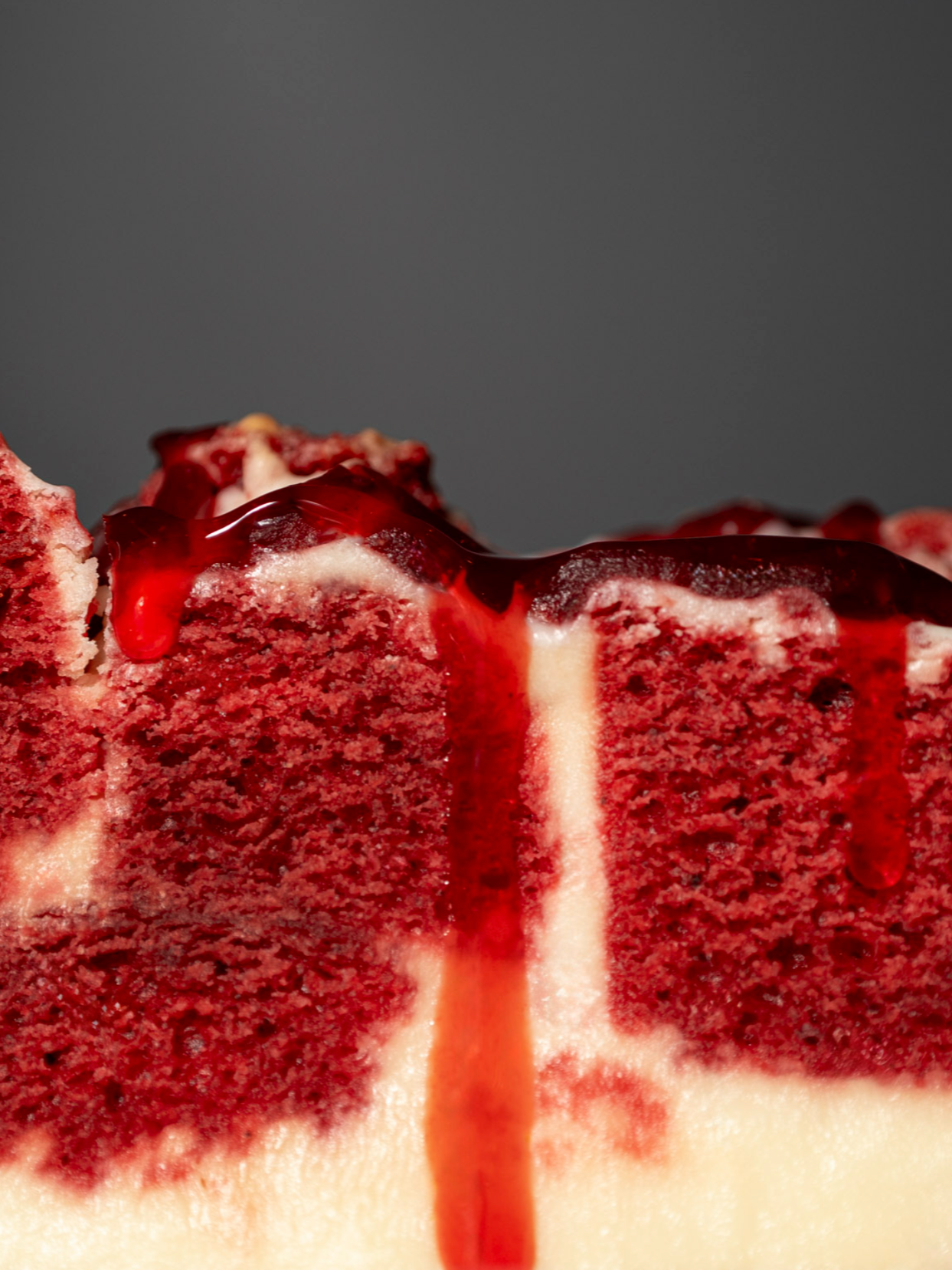 Close-up of a slice of red velvet cake with cream cheese frosting and red fruit glaze on top.