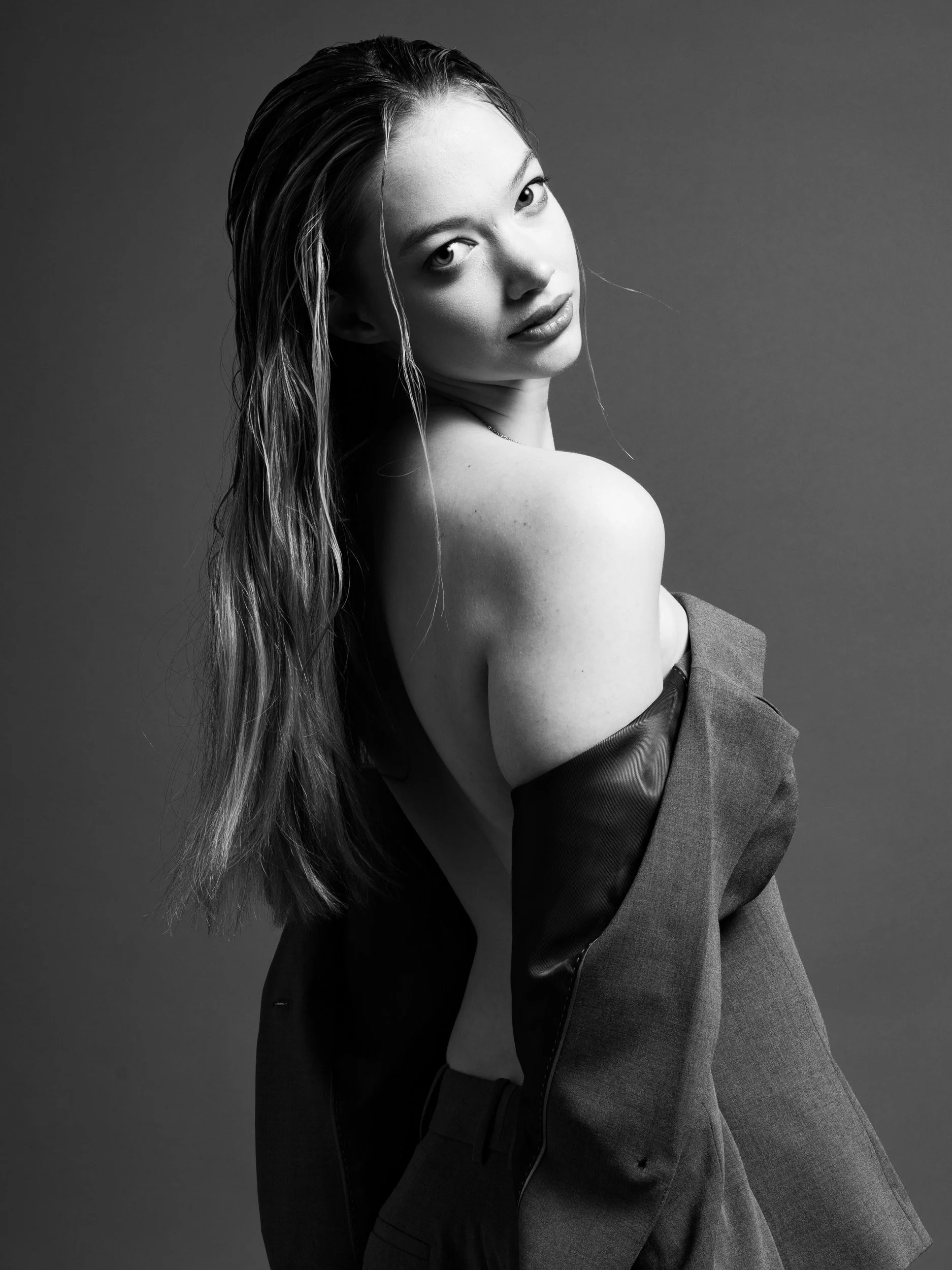 Black and white photo of a woman with long wet hair, looking over her shoulder at the camera, wearing a blazer.