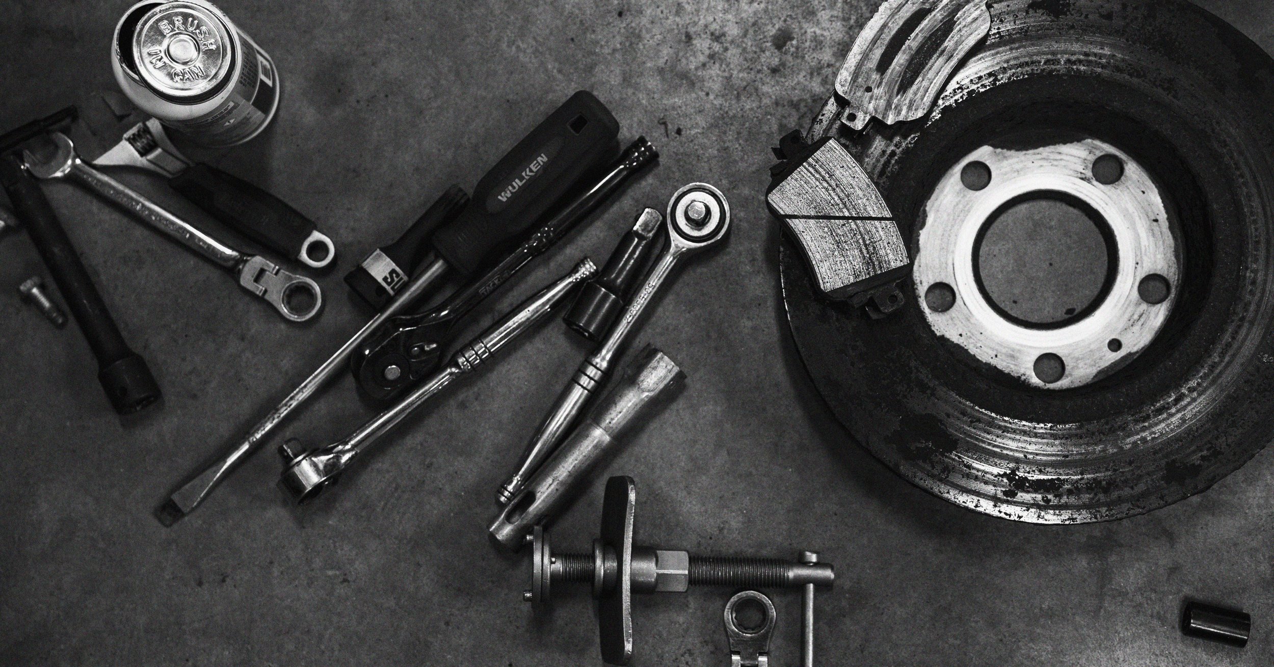 Various car tools and parts, including a brake disc and caliper, laid out on a work surface.