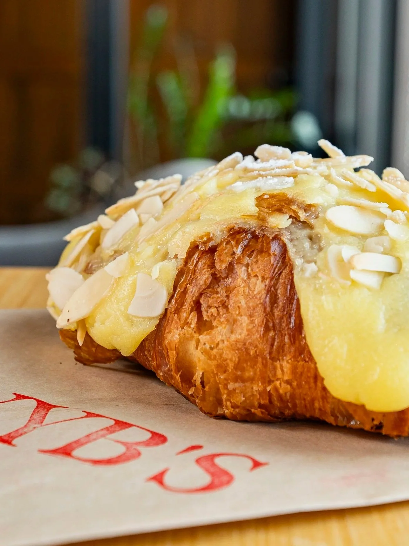 A close-up of a slice of almond croissant with visible almond slices and melted yellow custard, placed on a paper-lined surface.