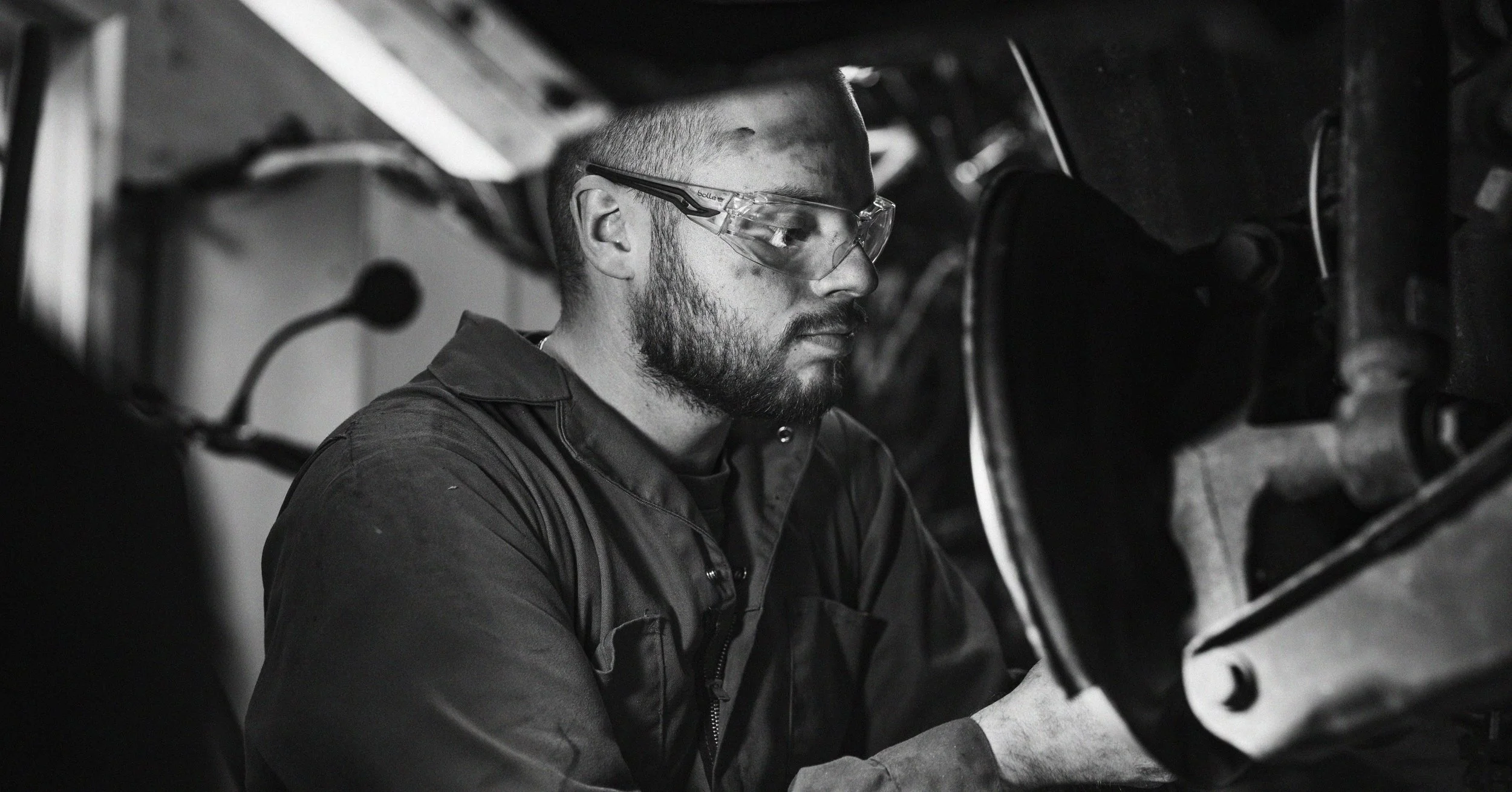A man wearing safety goggles working on mechanical equipment in a garage or workshop.