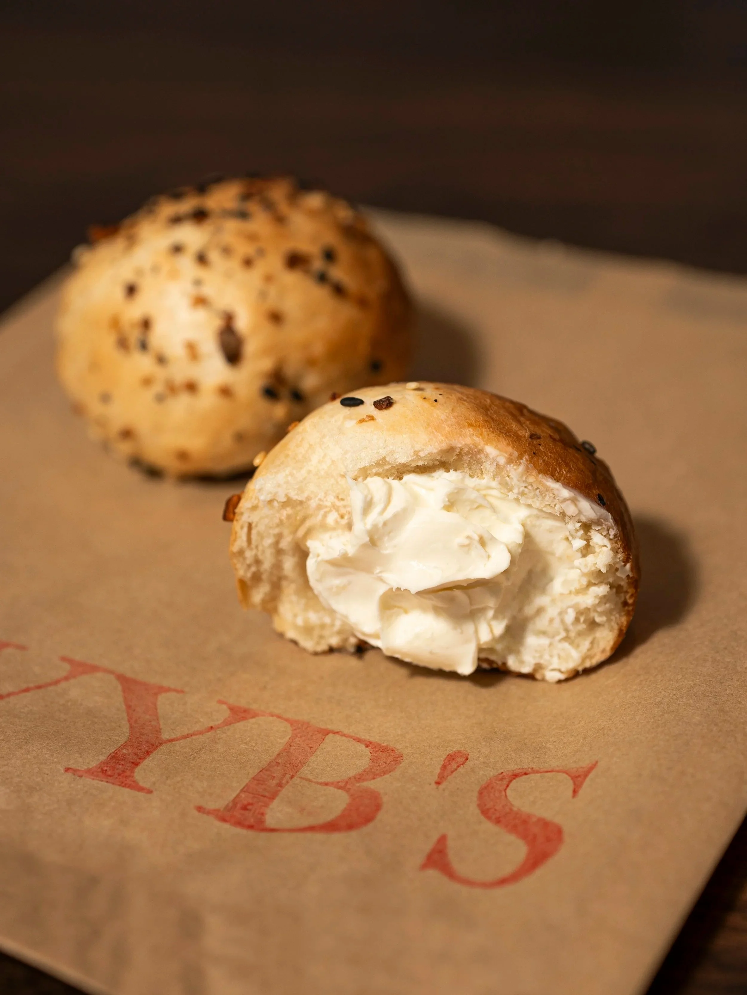Close-up of a partially eaten cream-filled pastry with a golden-brown crust topped with black sesame seeds, placed on brown paper with red printed letters.