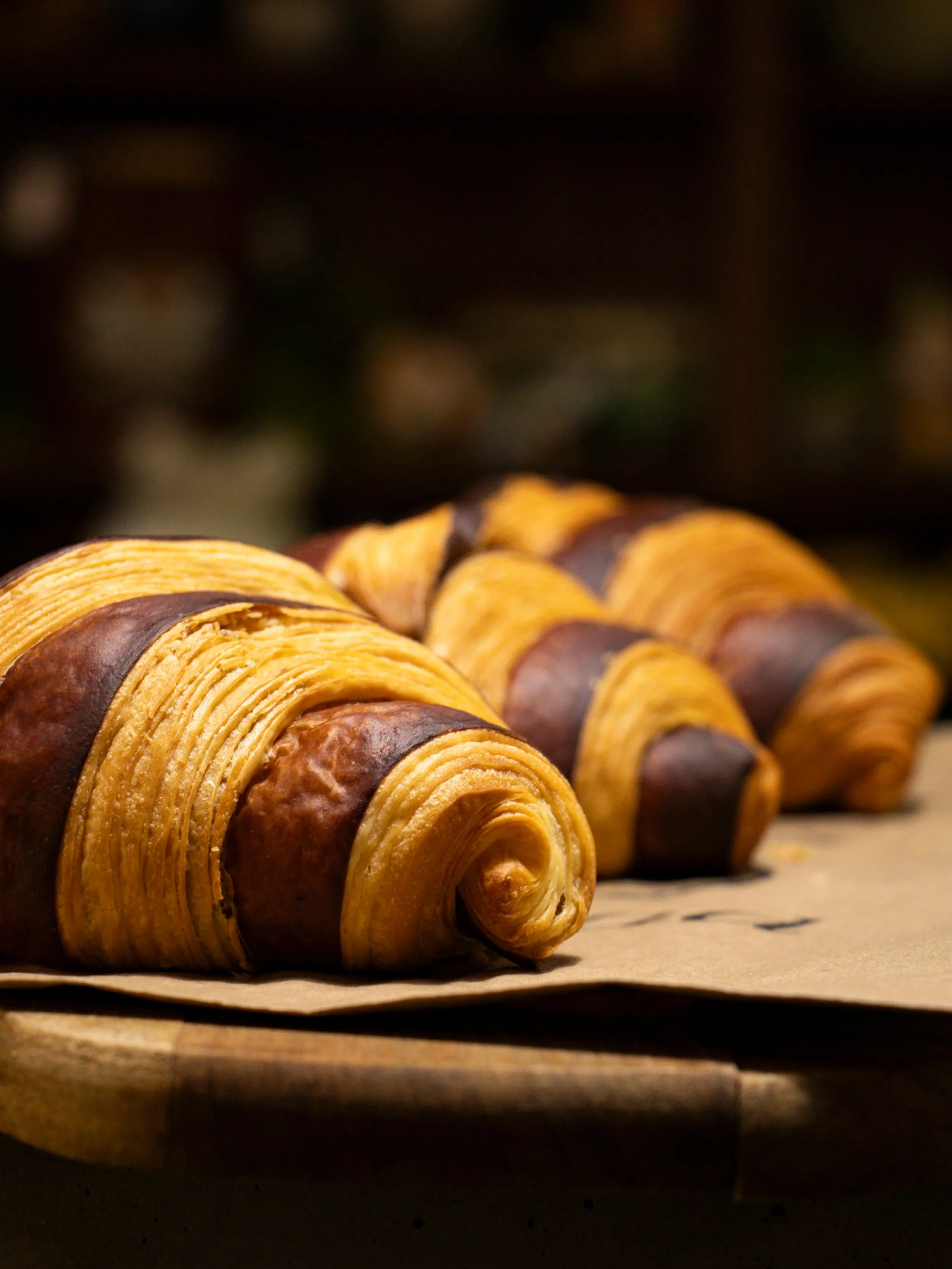Close-up of a row of baked croissants on a baking sheet, with a dark and blurred background.