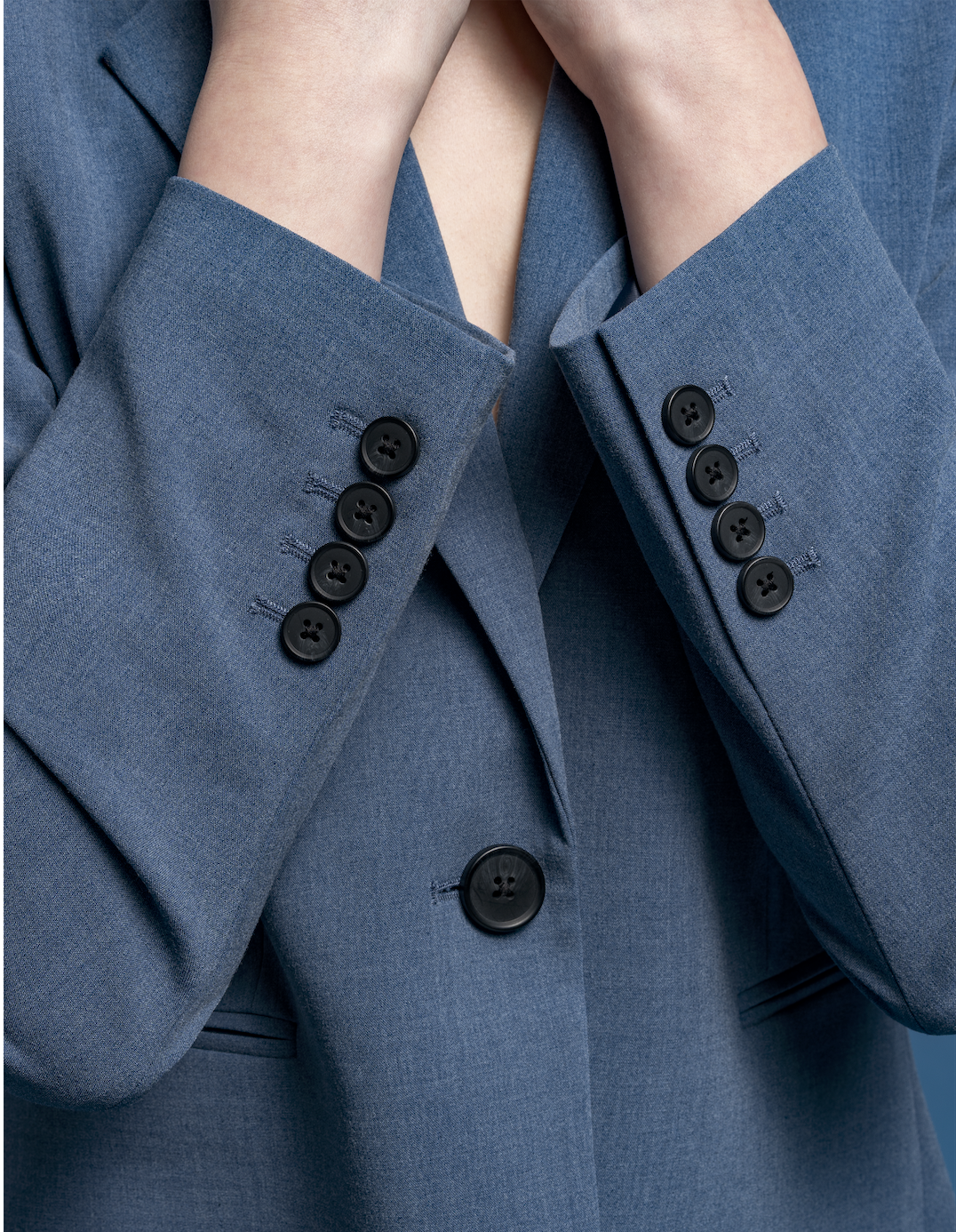 Close-up of a person wearing a blue suit with black buttons, with hands touching face.
