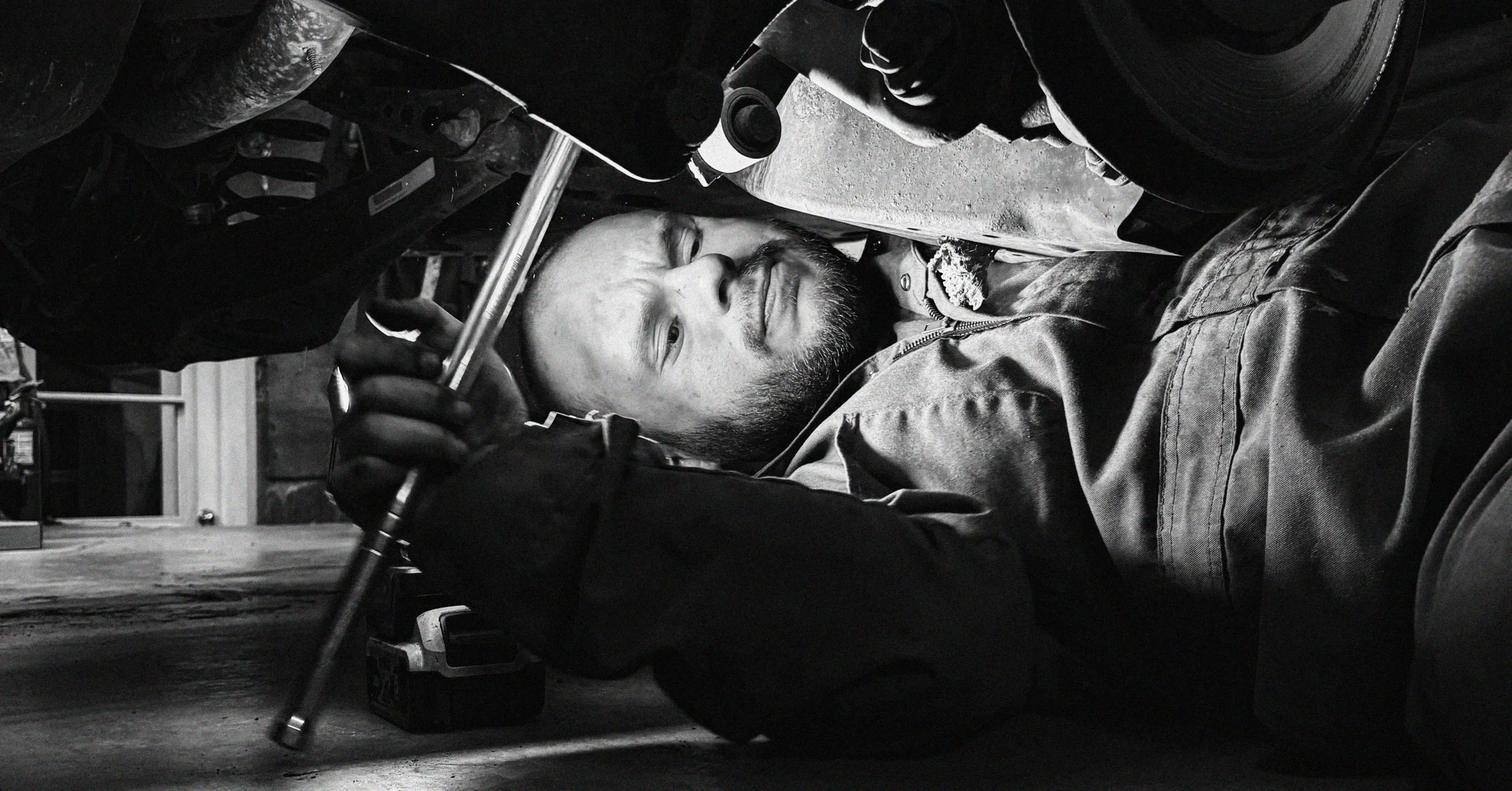A mechanic working underneath a car, lying on the ground in a garage.