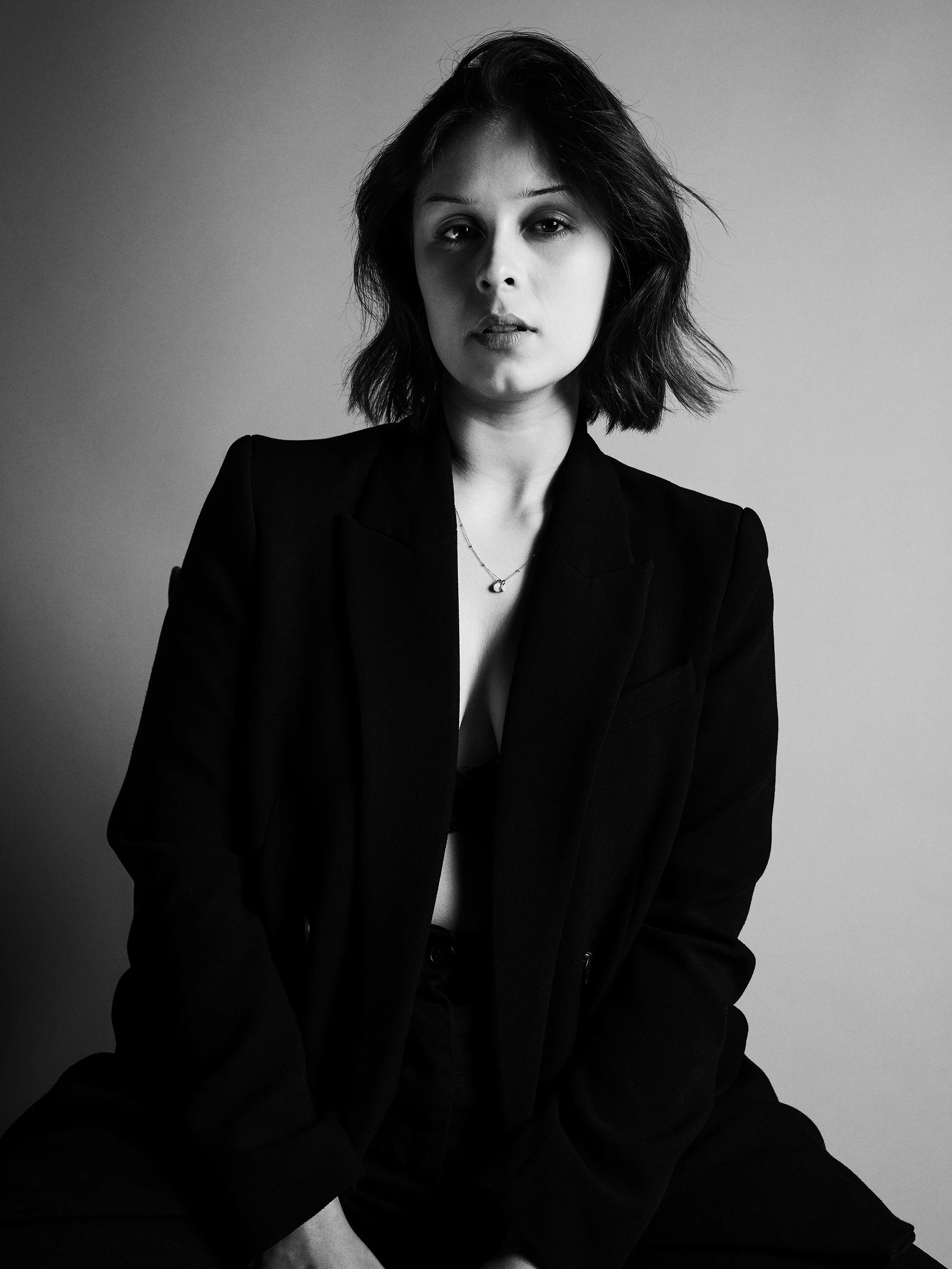 Black and white photo of a woman with shoulder-length dark hair, wearing a blazer, sitting against a plain backdrop, with a serious expression.