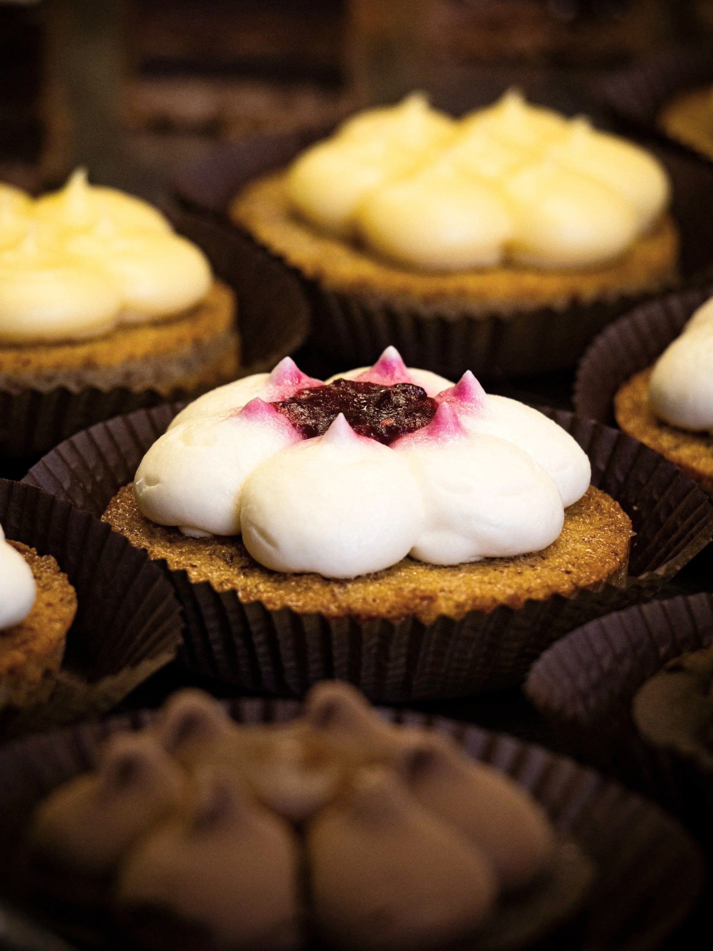 Close-up of assorted cupcakes with different toppings, including one with cream and fruit preserves.