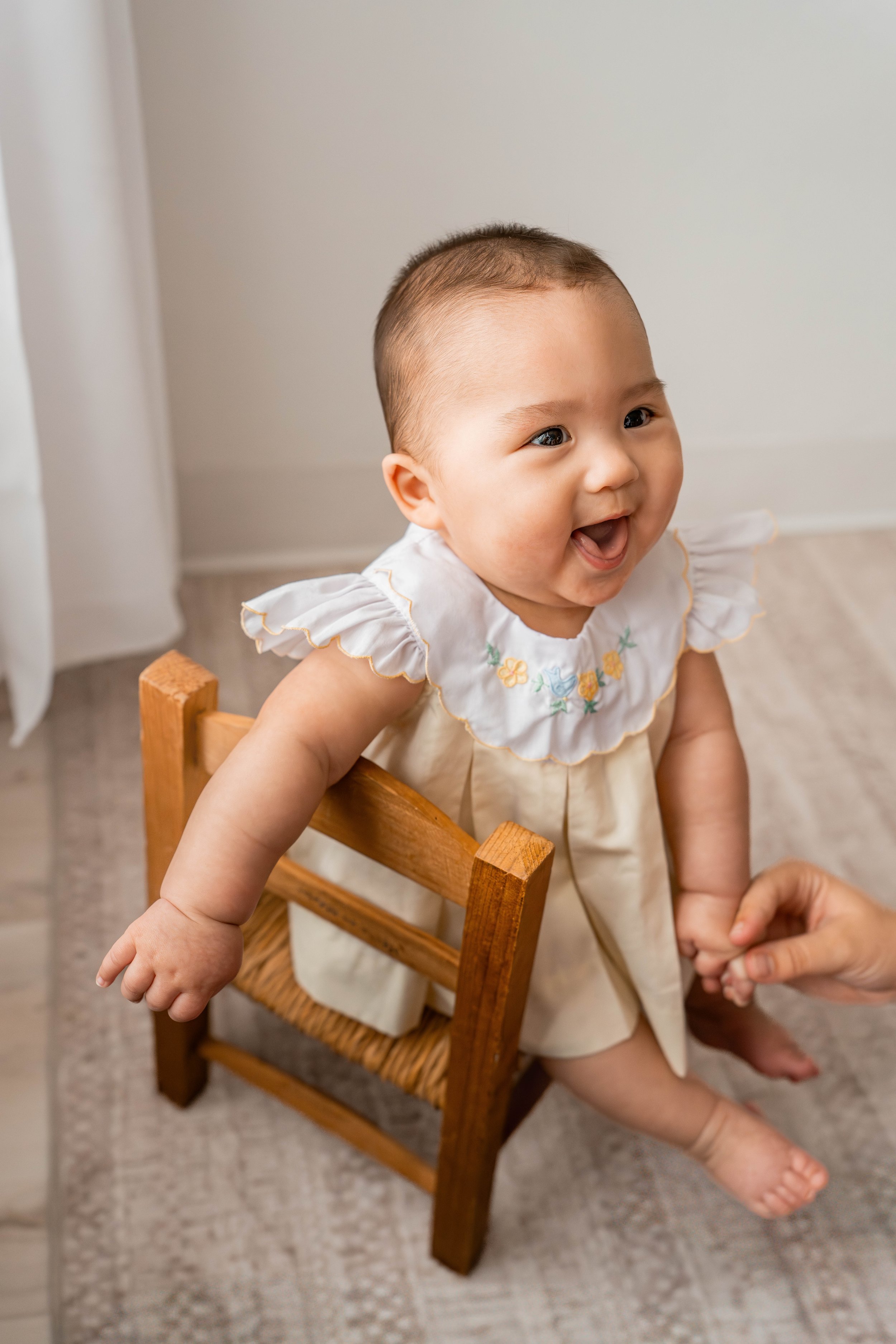 Baby girl smiling in a wooden chair during her 6-month studio milestone session in Beavercreek, Ohio