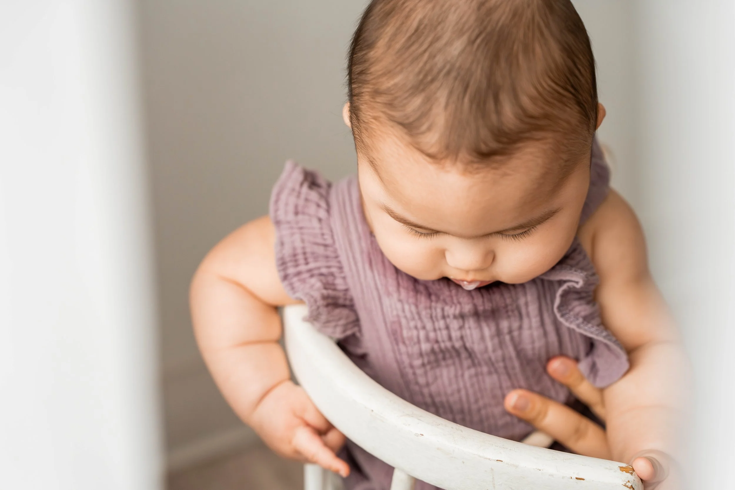 Baby girl drooling on her purple outfit while sitting in a white chair