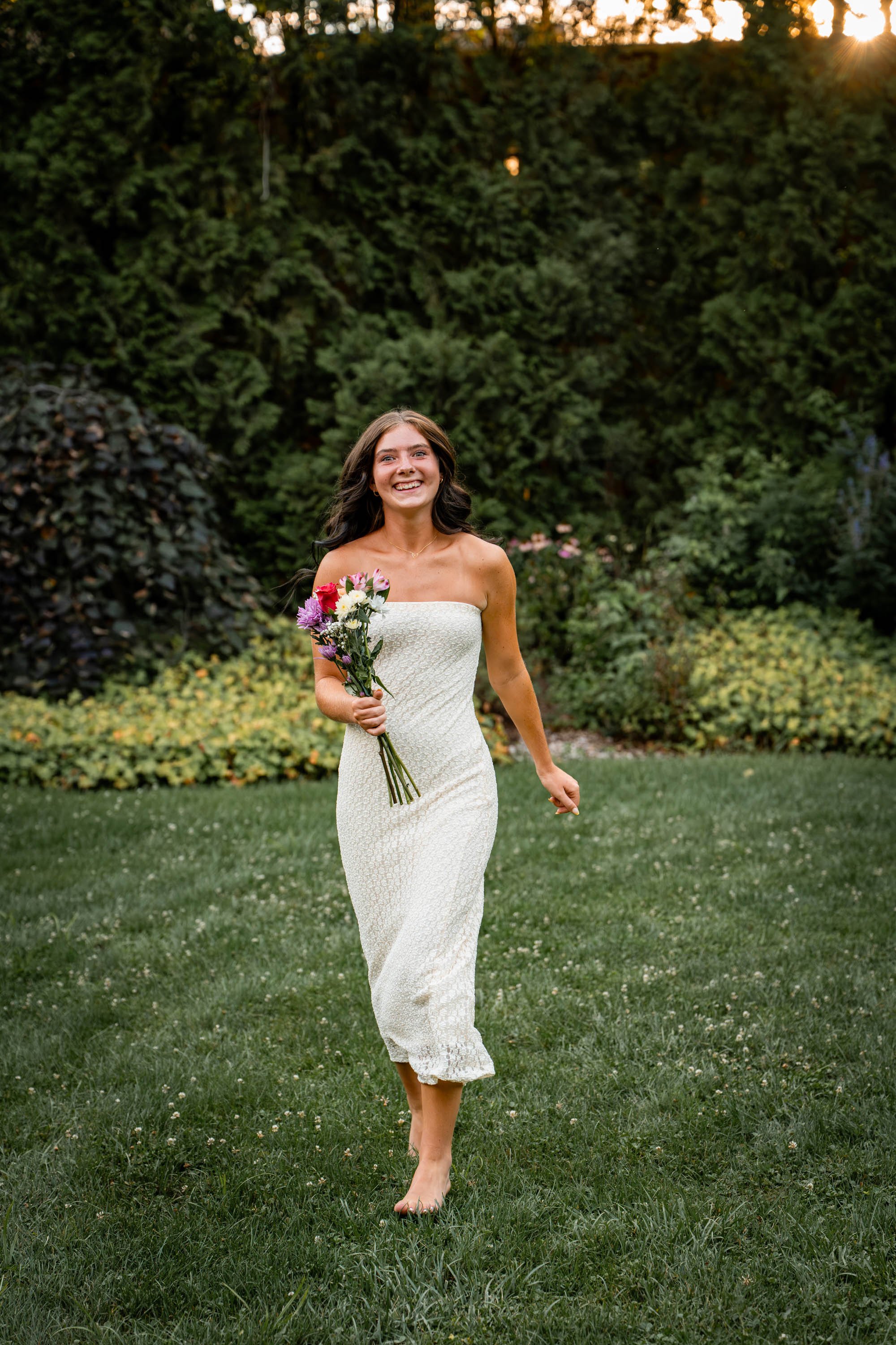 senior girl in a white dress runs through a field with flowers