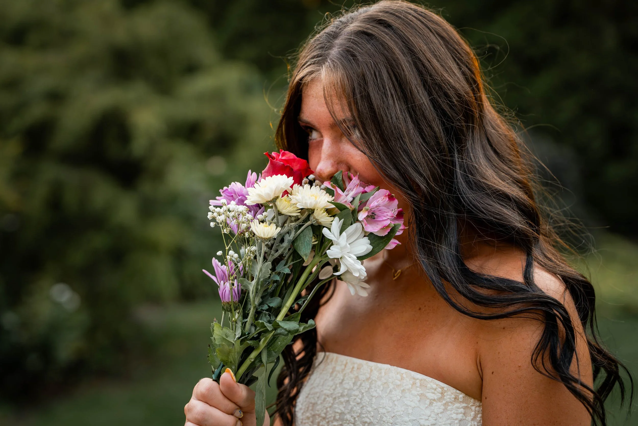 girl in a white dress with long brown hair smells flowers