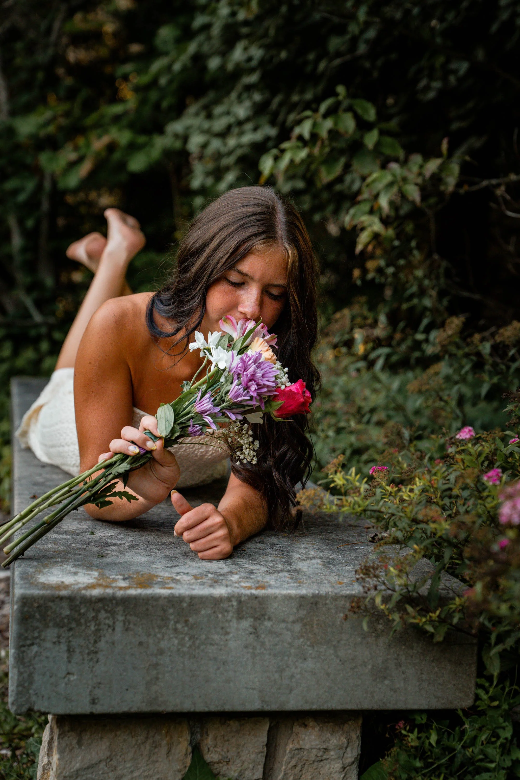 a girl wearing a white dress lays on a bench with flowers