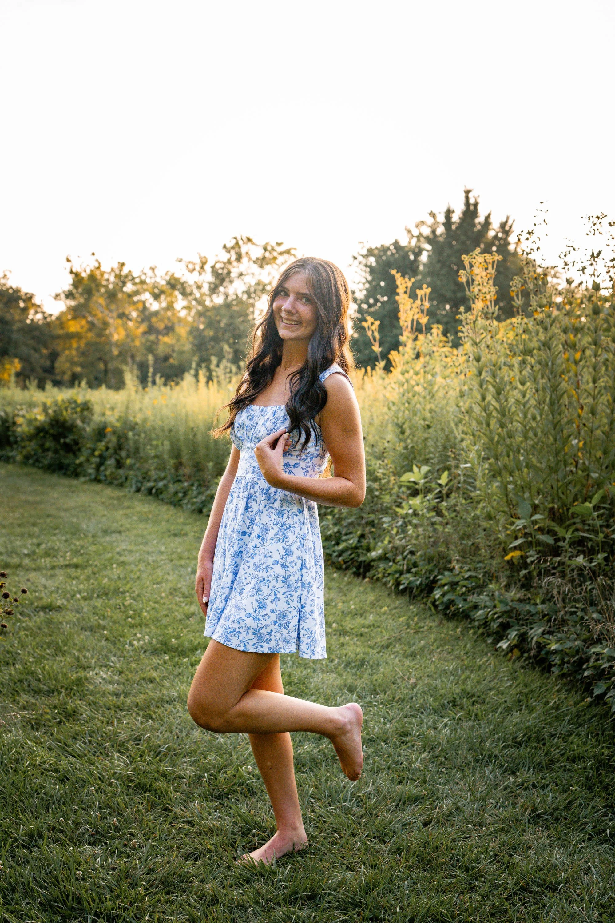 a girl stands barefoot in a blue and white dress in a field at Wegerzyn Gardens