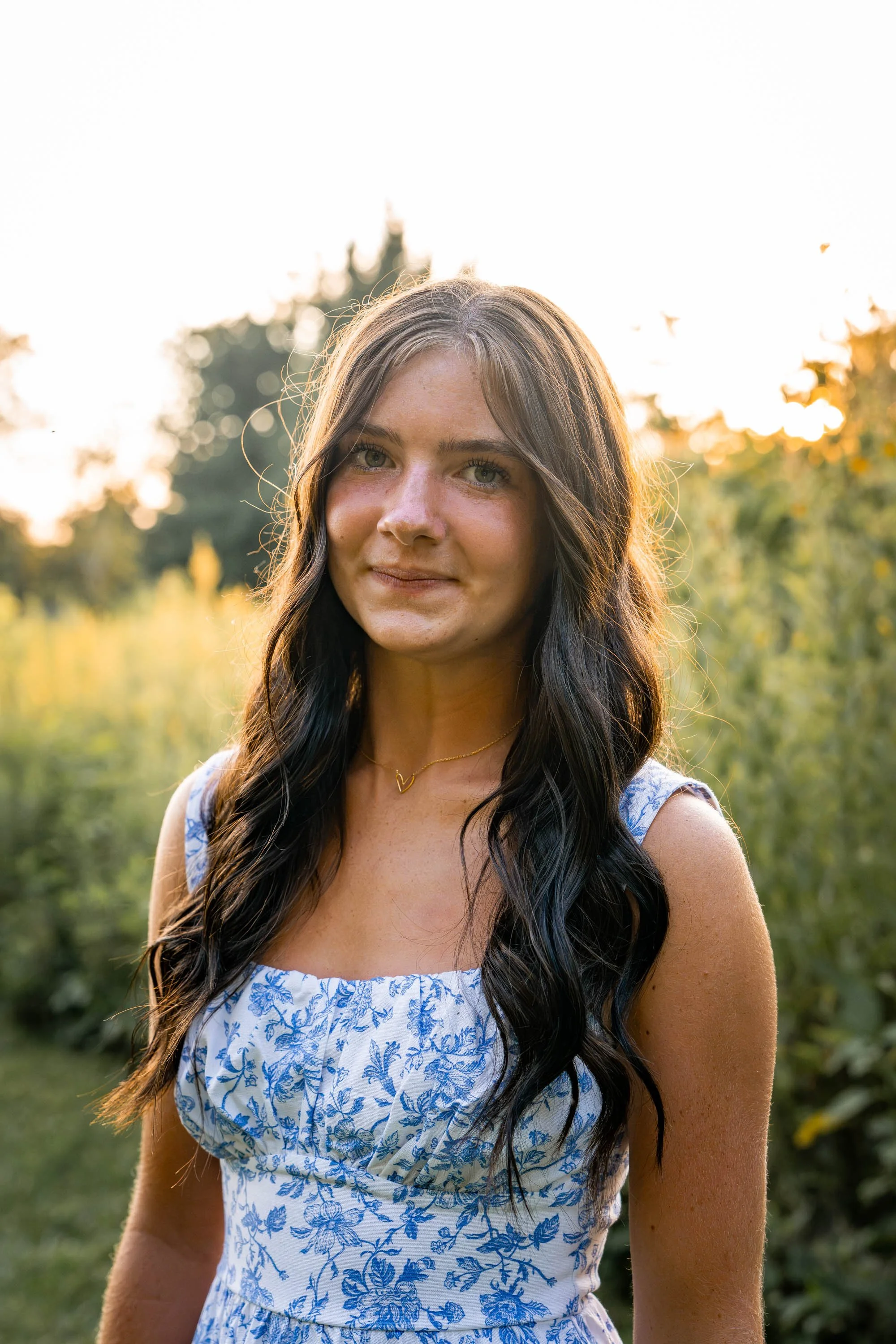 a girl lightly grins at the camera while wearing a blue and white dress standing in a wildflower field