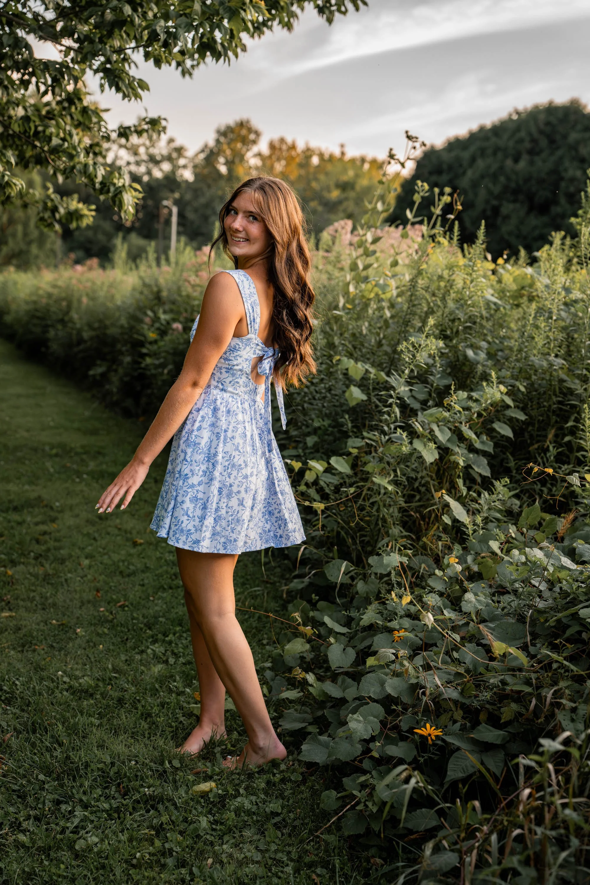 a girl stands beside the wildflowers in a blue and white dress twirling back and forth