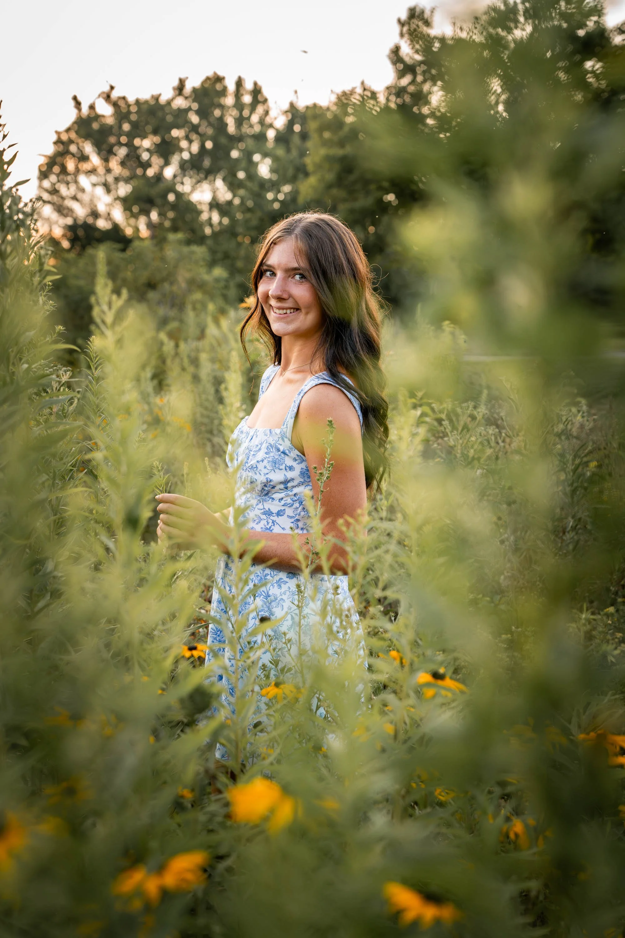 a girl wearing a blue and white dress stares at the camera through the stems of the wildflowers in Dayton Ohio