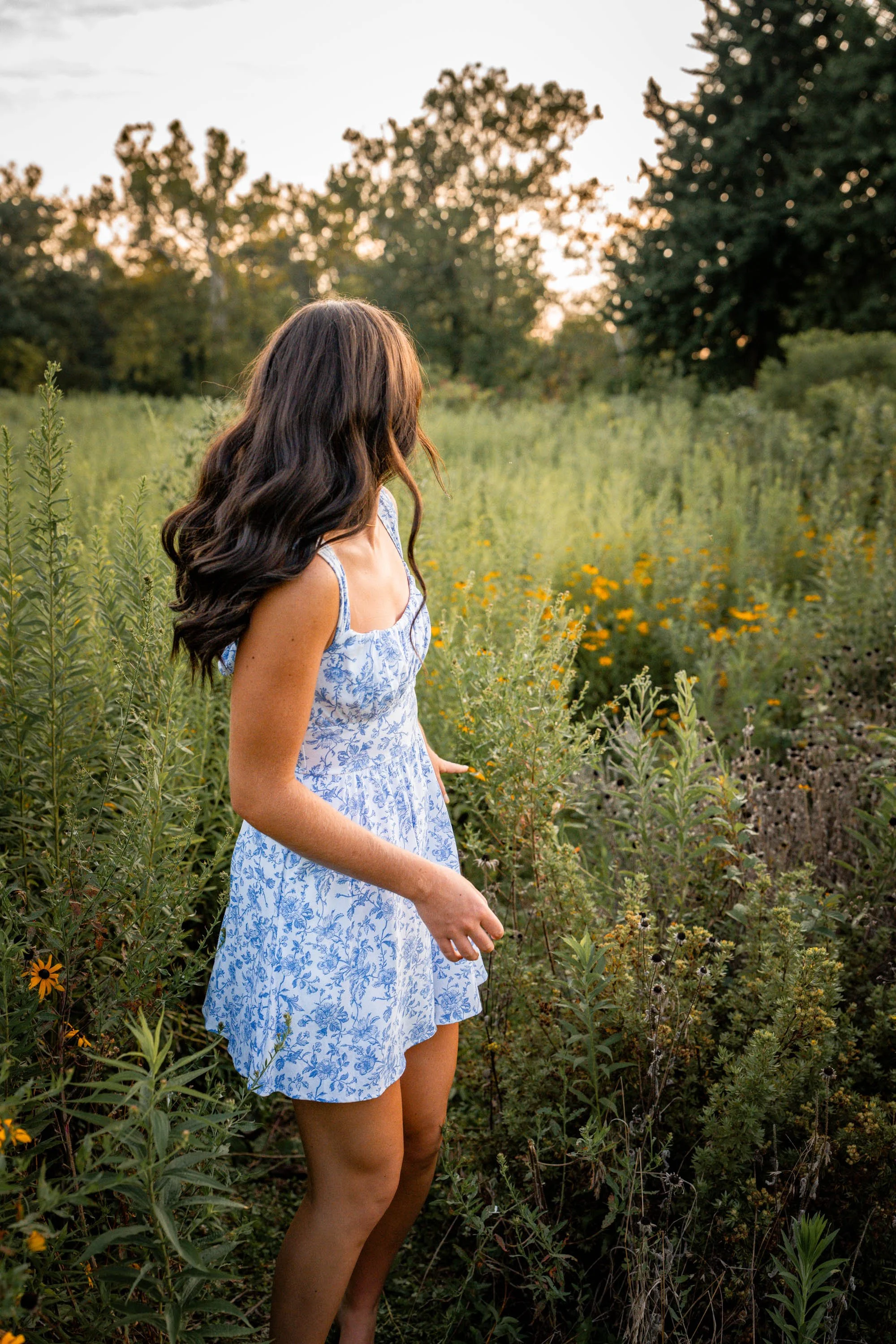 a senior girl appears to be turning away quickly as if to run through a field of wildflowers