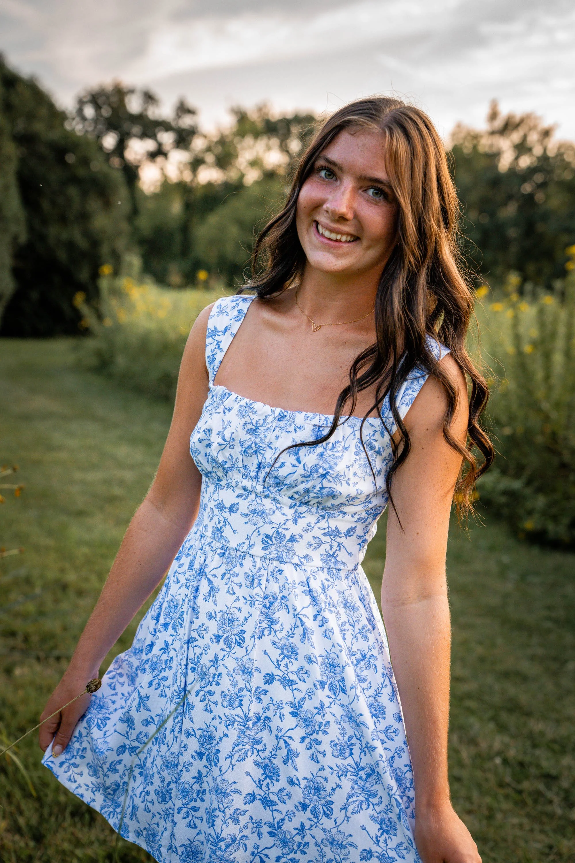 a girl wearing a dress pulls it out as if to curtsey as she walks toward the camera out of the wildflower field 