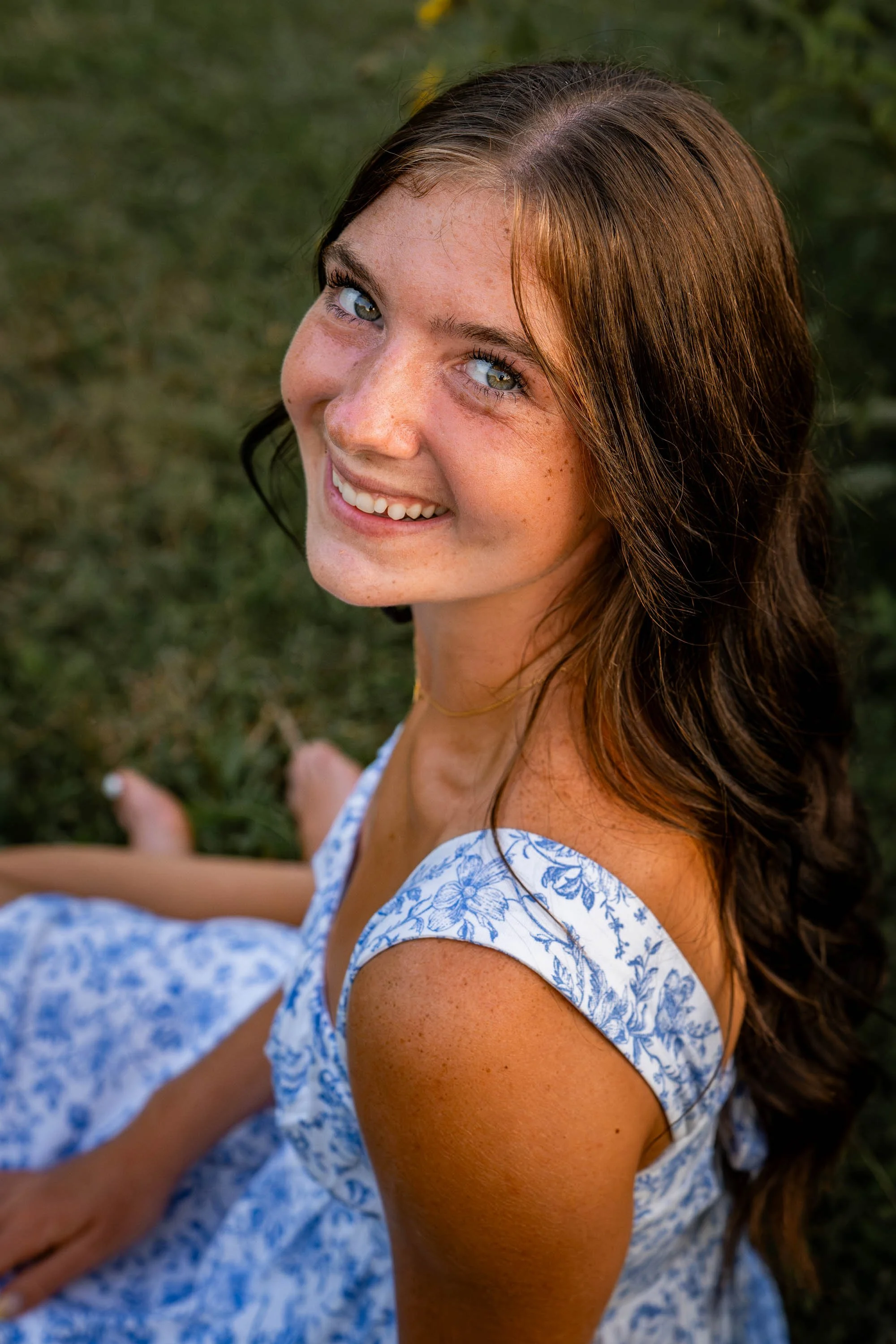 a girl sits in the grass looking back at the camera and smiling