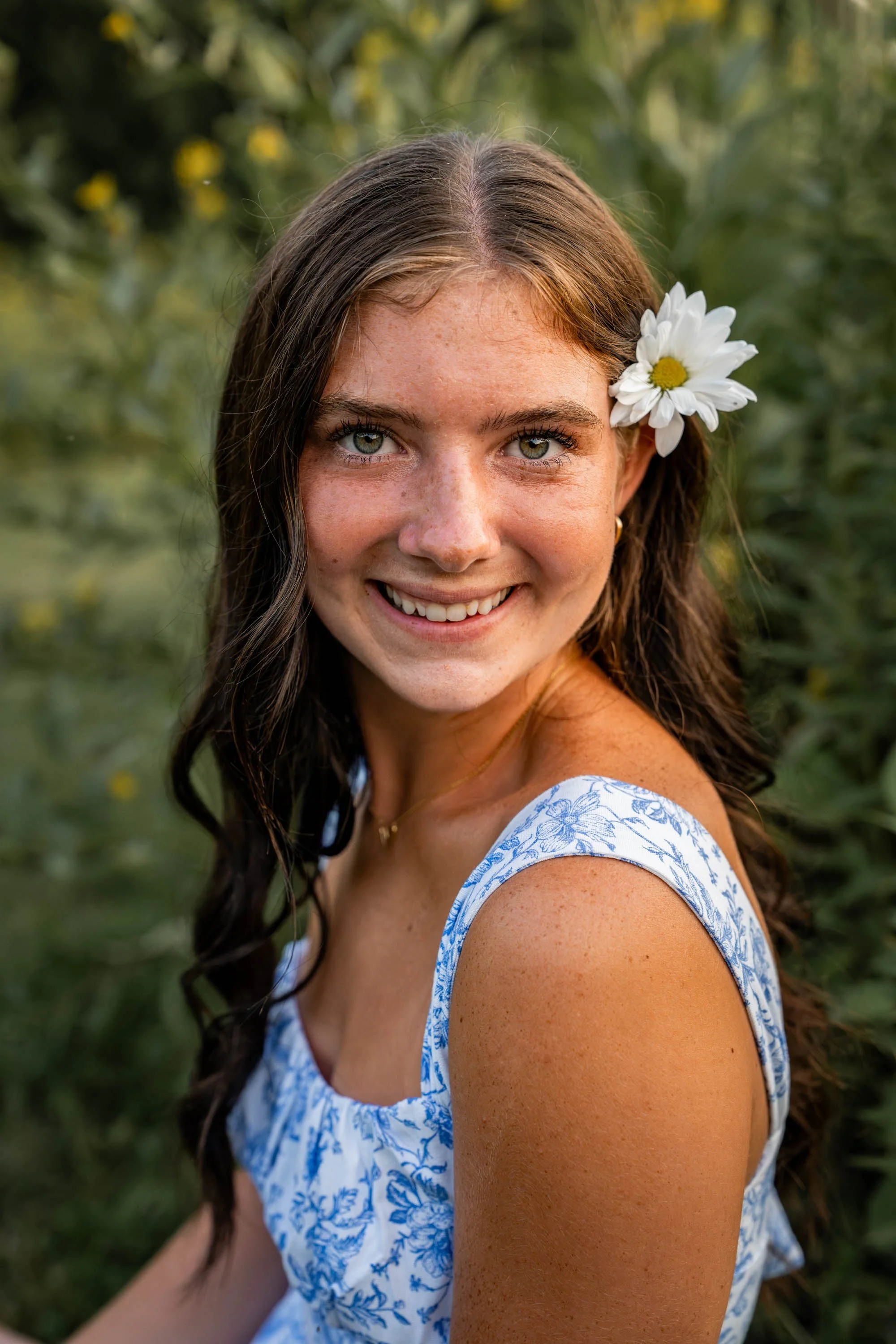 senior girl sits in the grass with a white flower in her hair at a park in Dayton Ohio