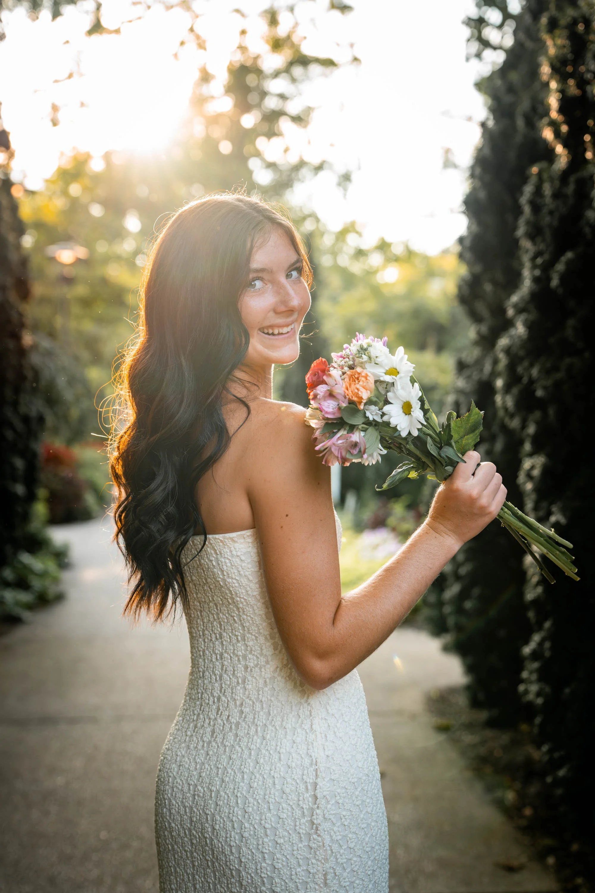 Senior girl in a white dress with flowers and glowy sunlight