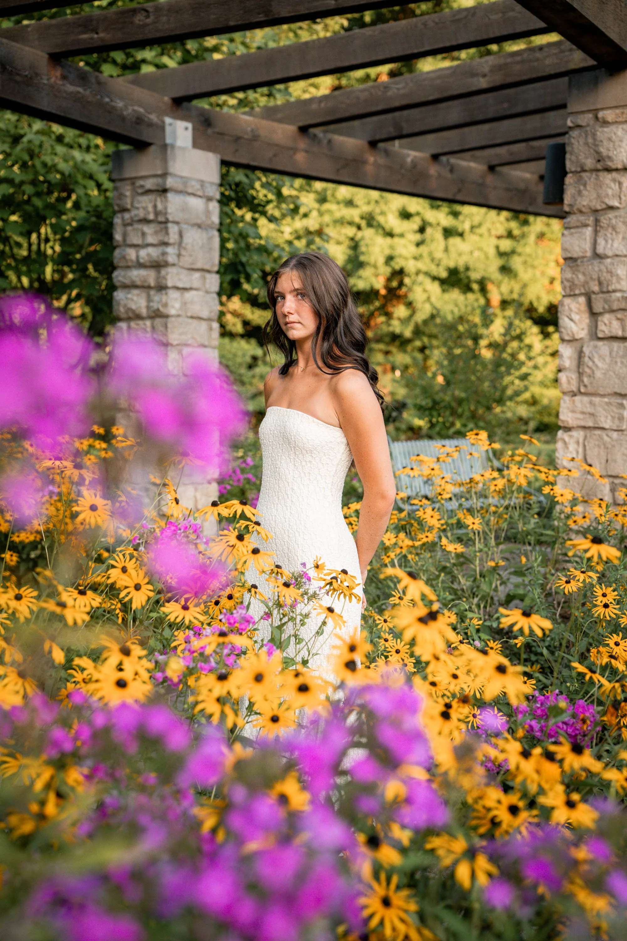 senior girl poses in a garden with pink and yellow flowers