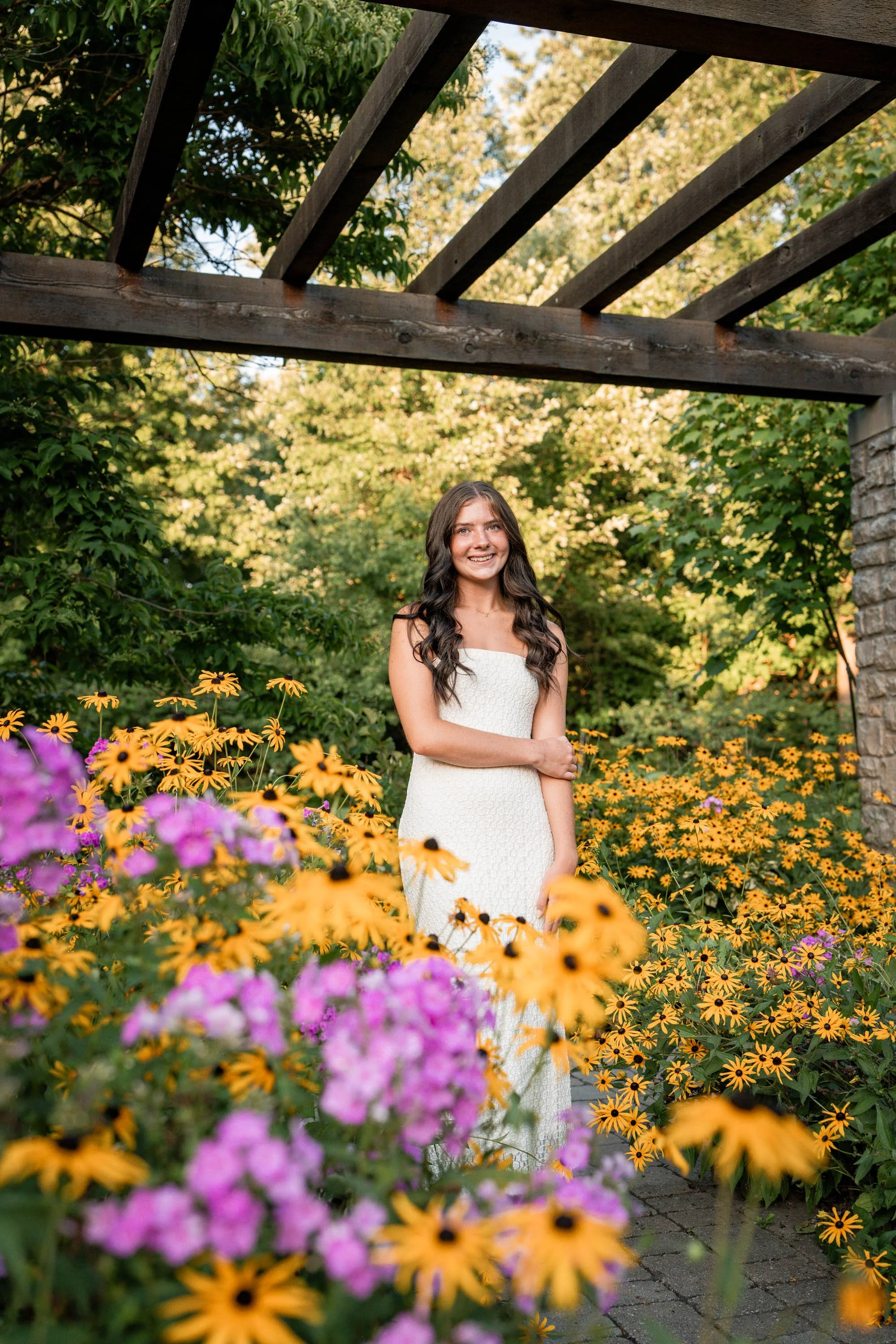 senior girl at Wegerzyn Garden in Dayton Ohio poses by the stone wall and pink and yellow flowers