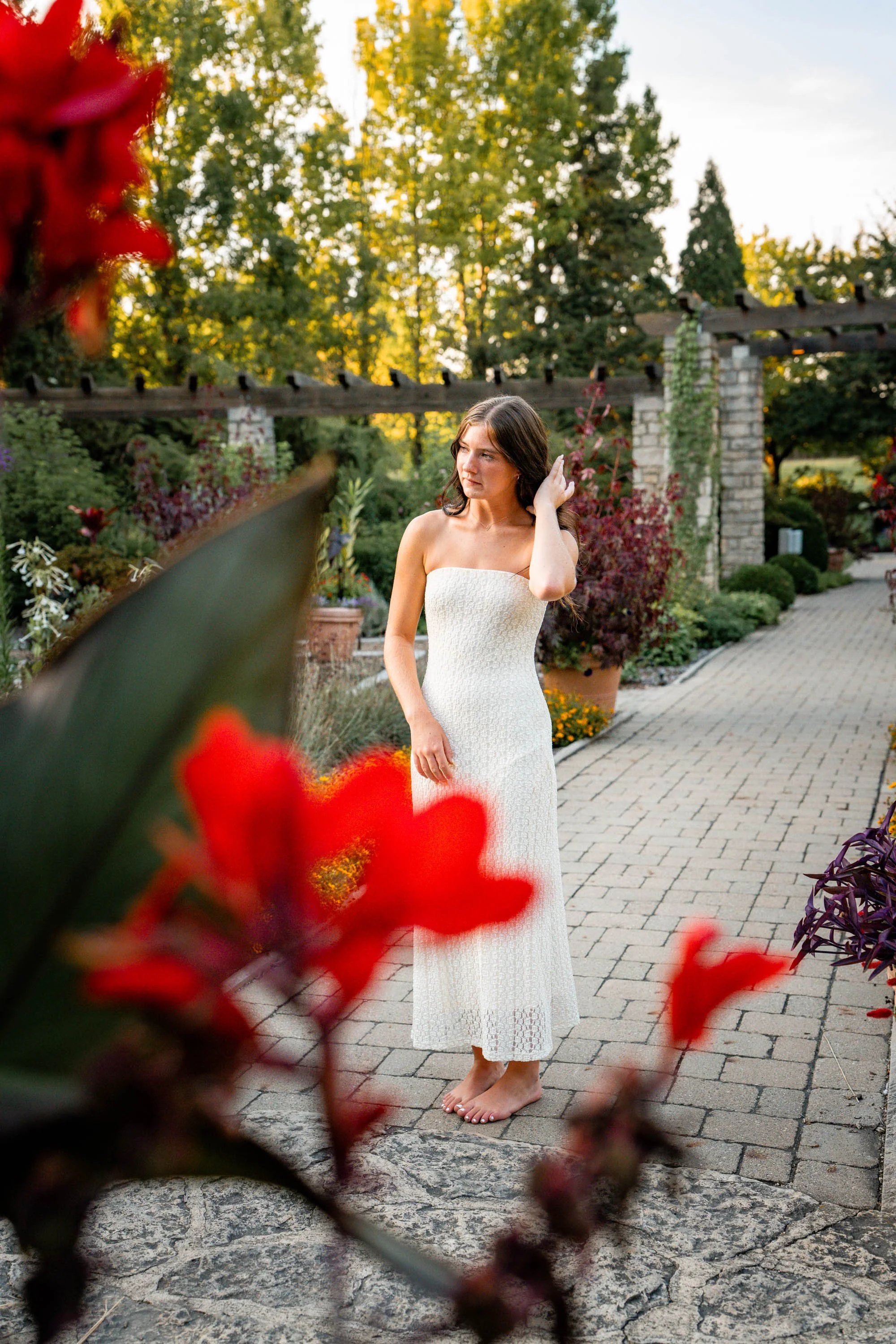 Senior girl in a white dress runs her fingers through her hair amidst red blooms in the garden in Dayton Ohio