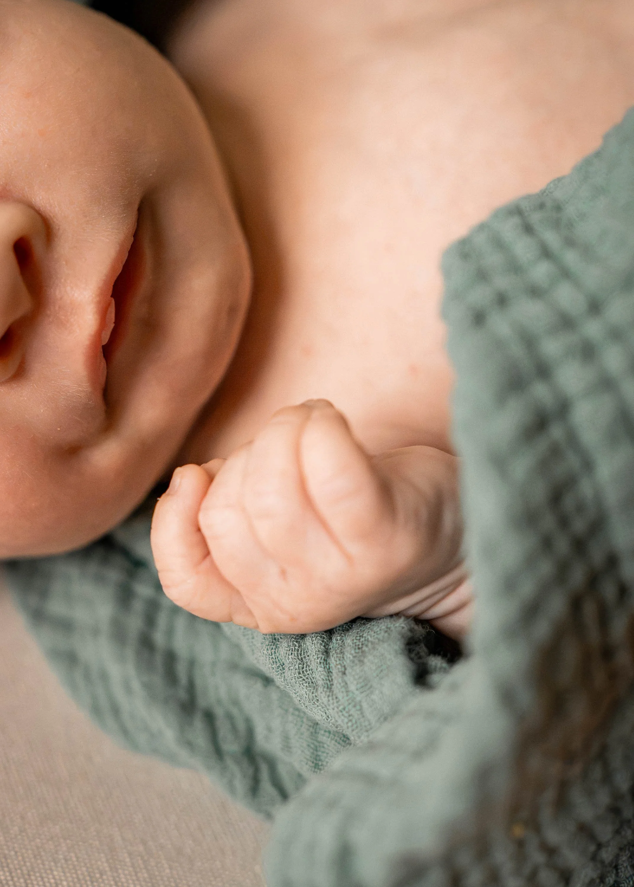 a closeup shot of a baby boy's hand who is wrapped in a green swaddle