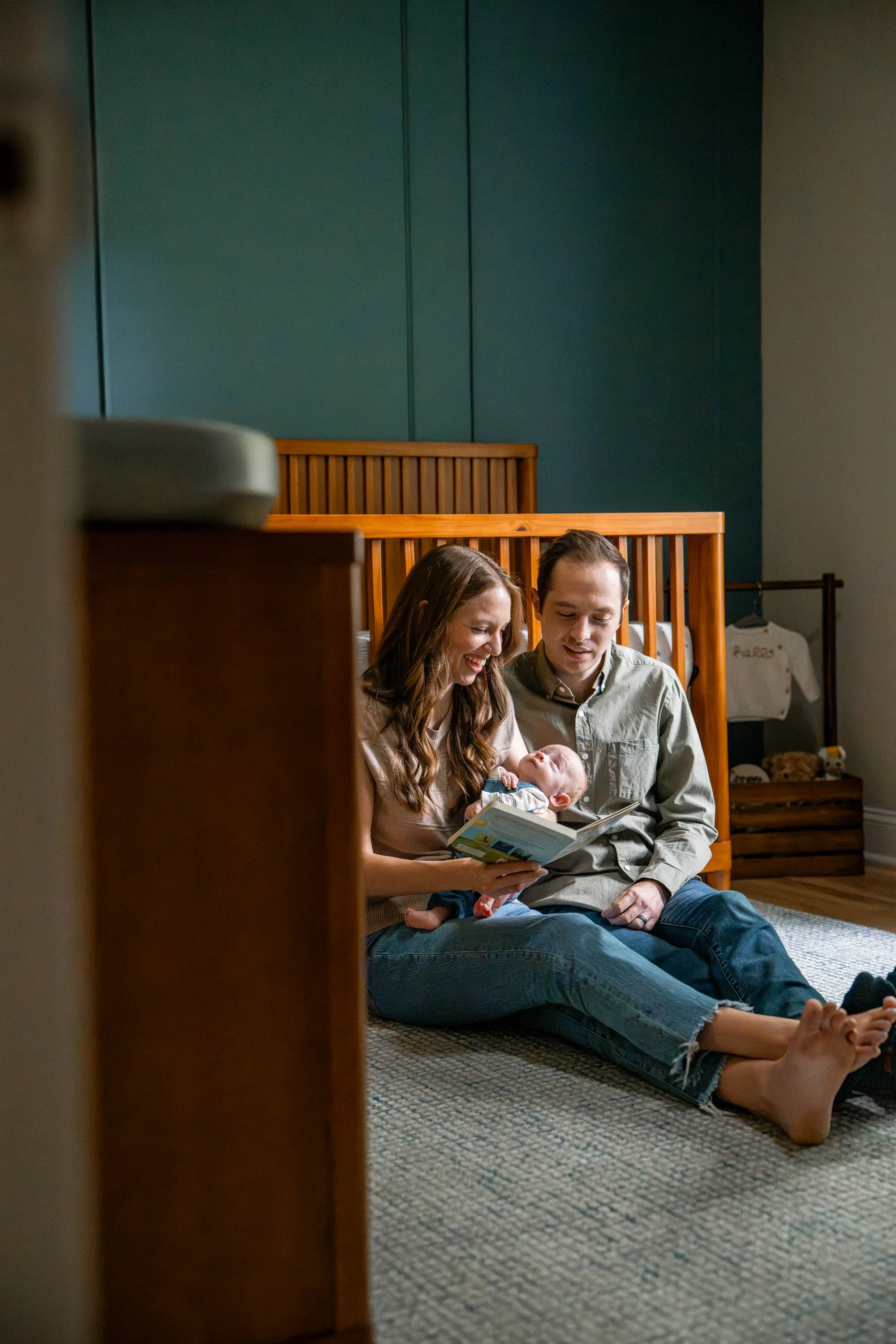 New parents sitting on the floor in the nursery reading their baby a book in Beavercreek Ohio