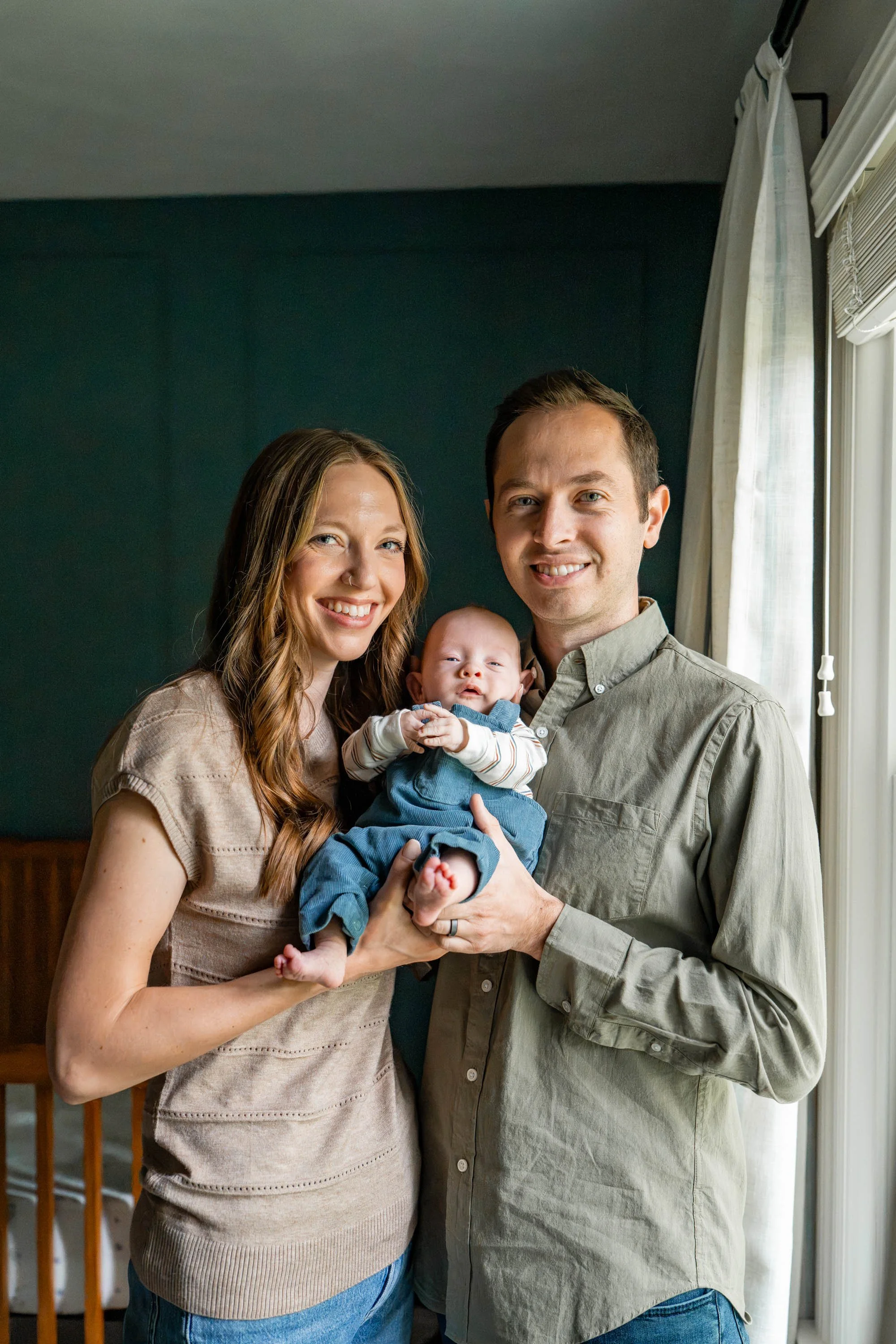 Mom and dad smiling with baby by the bedroom window