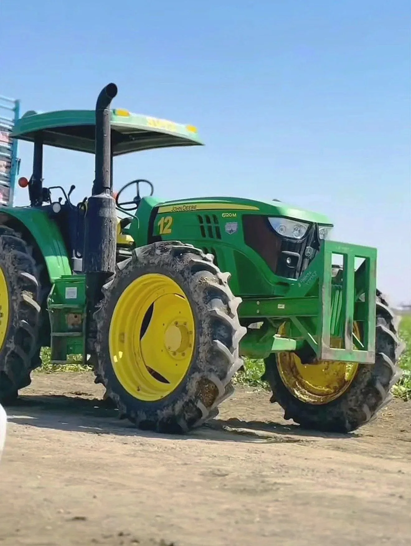 A green John Deere tractor on a dirt field under a clear blue sky.