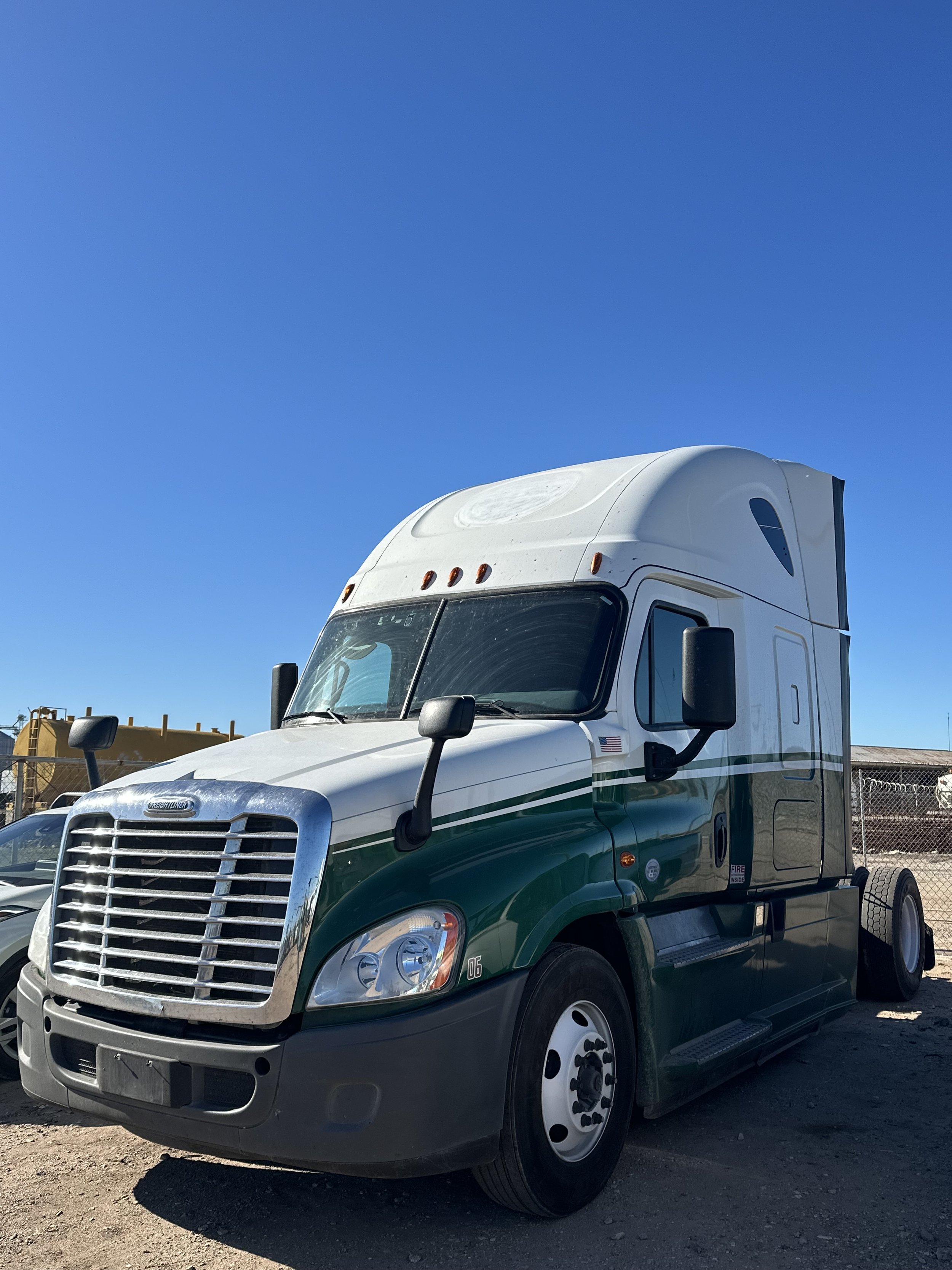A large white and green semi-truck with a high sleeper cab parked outside on a clear day.