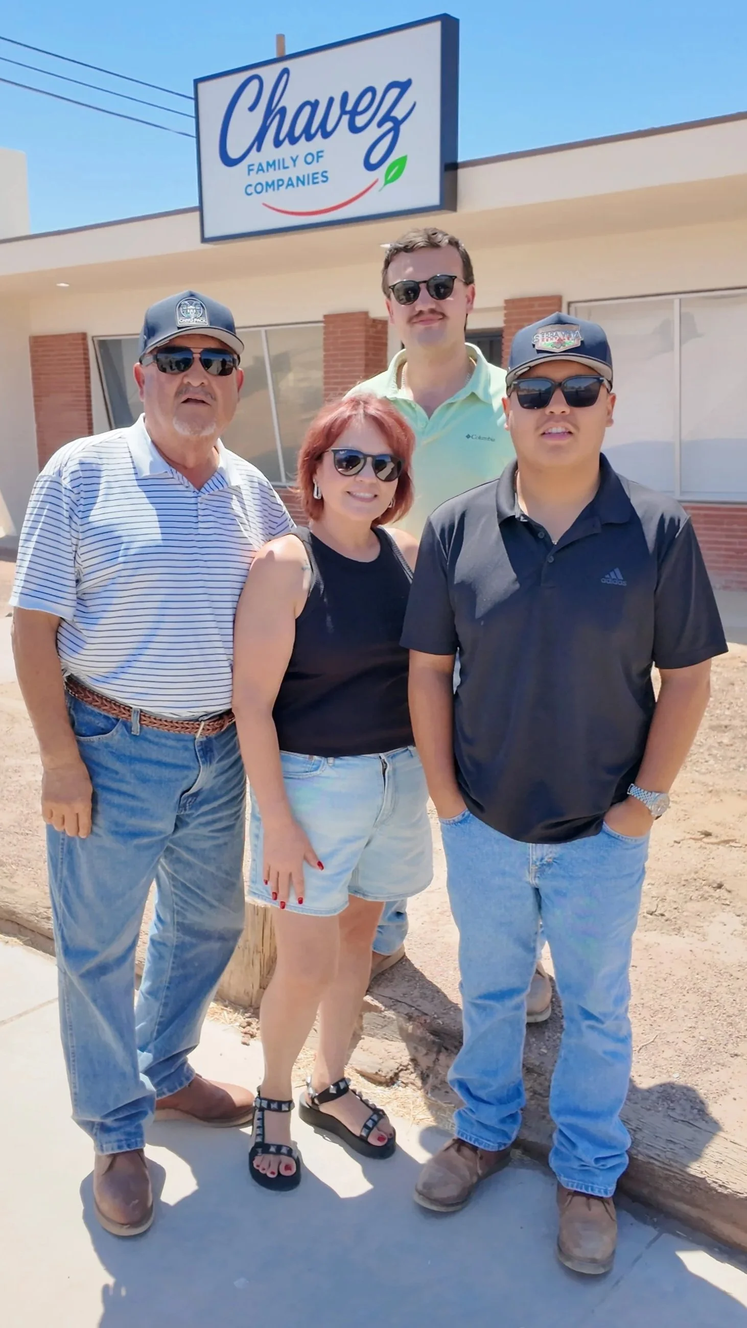 A group of five people standing outside a building with a sign that reads 'Chavez Family of Companies.'